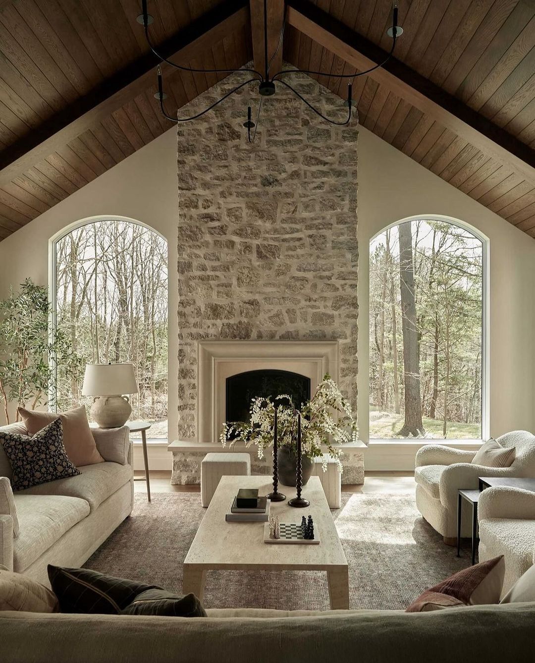 A cozy and inviting living room featuring a majestic stone fireplace and arched windows with a view of the woods