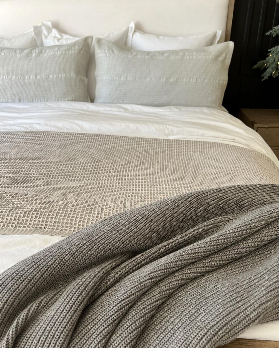 A neatly made bed with a textured grey throw at the foot