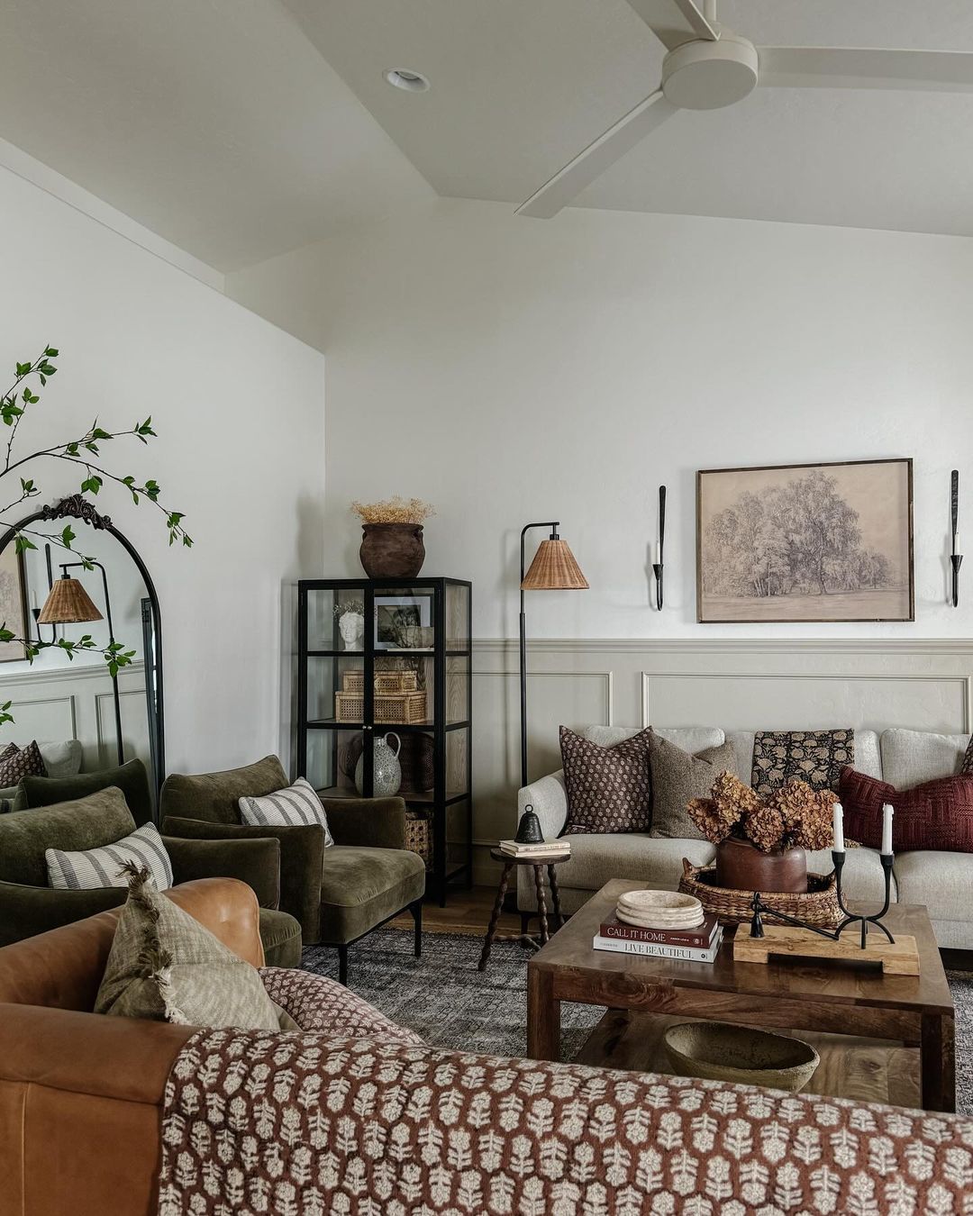 A cozy and well-appointed living room featuring lush green velvet armchairs, a caramel leather sofa, and rustic wooden accents.