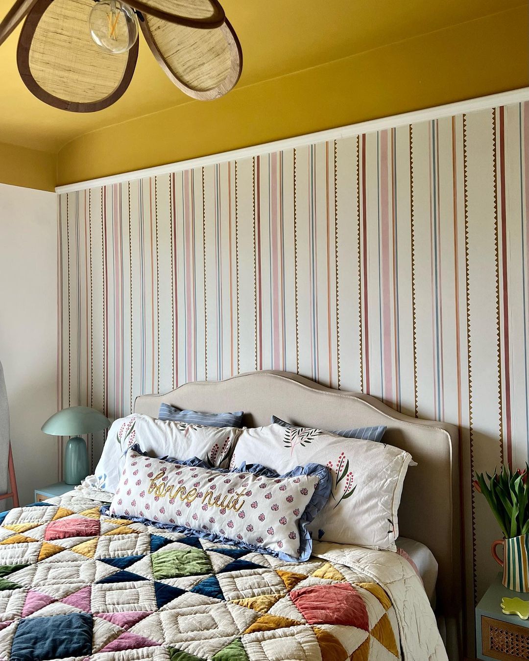 A cozy bedroom featuring a multicolored patchwork quilt and striped wallpaper