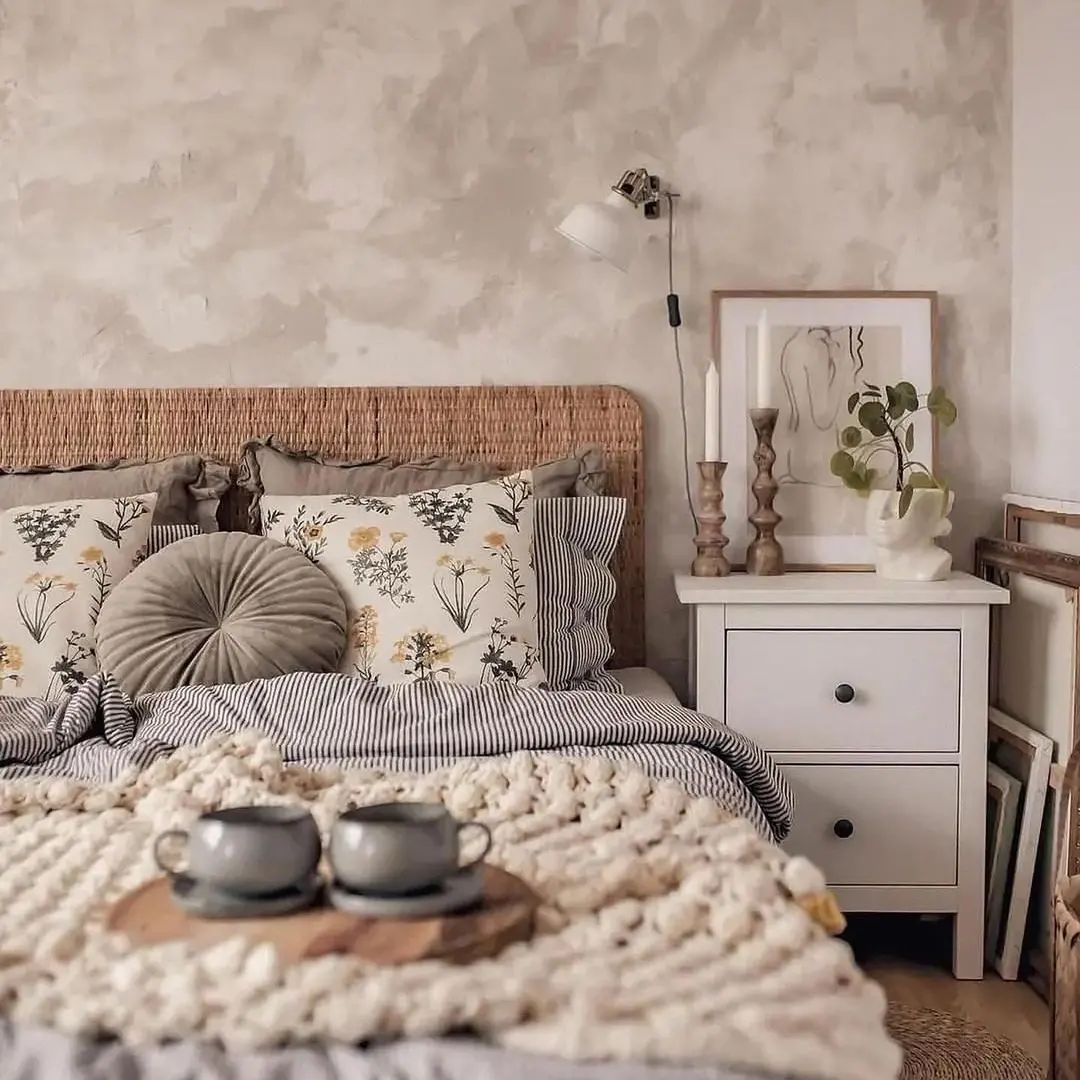 A harmoniously layered bedroom featuring a rattan headboard, floral and striped linens, and a chunky knit throw