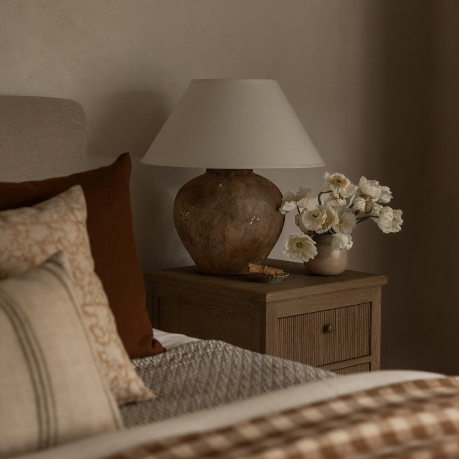 A cozy bedroom corner featuring earth tones with a textured bedspread and a wooden nightstand.