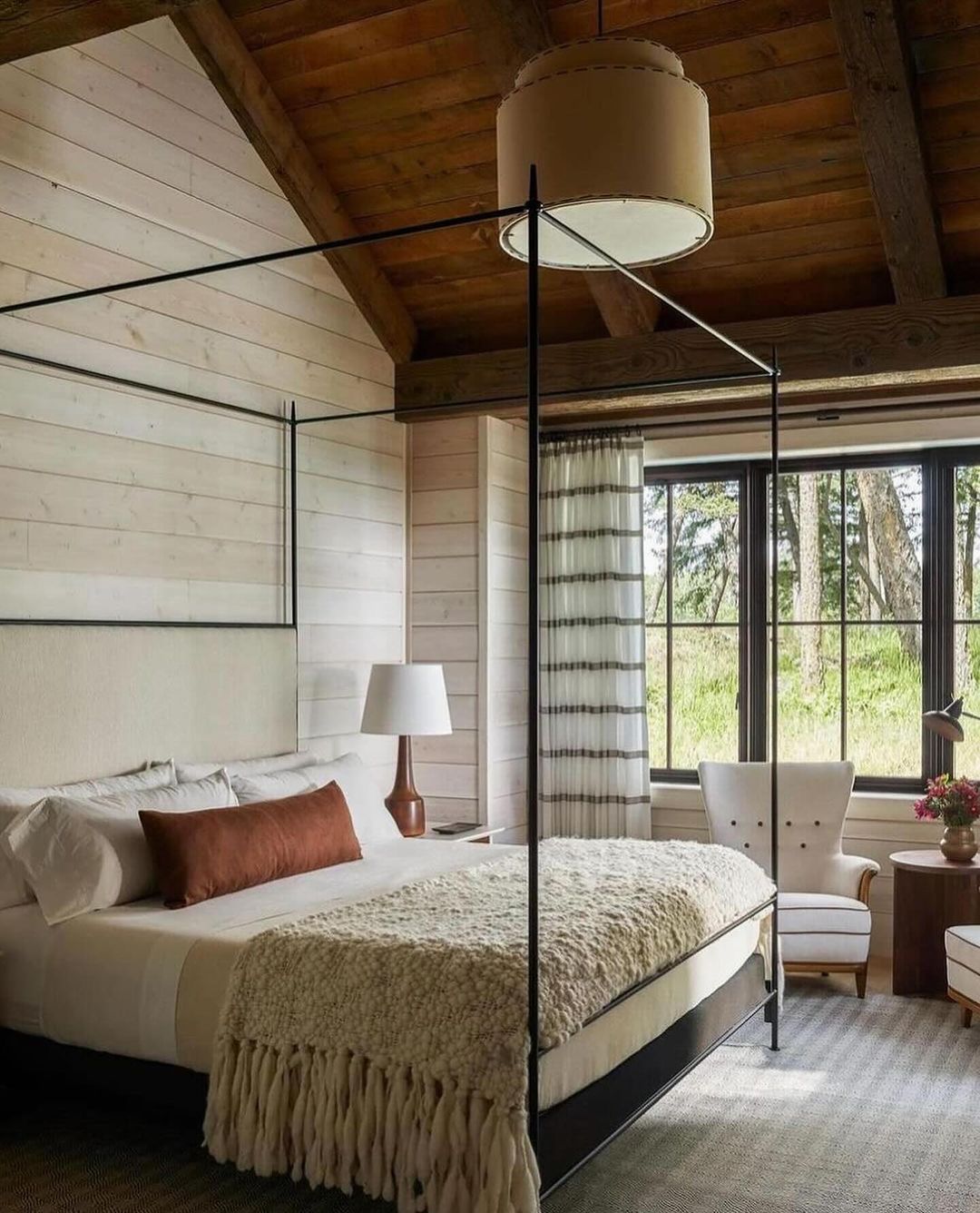 A cozy and inviting bedroom featuring shiplap walls, rustic wooden ceiling beams, and a four-poster bed