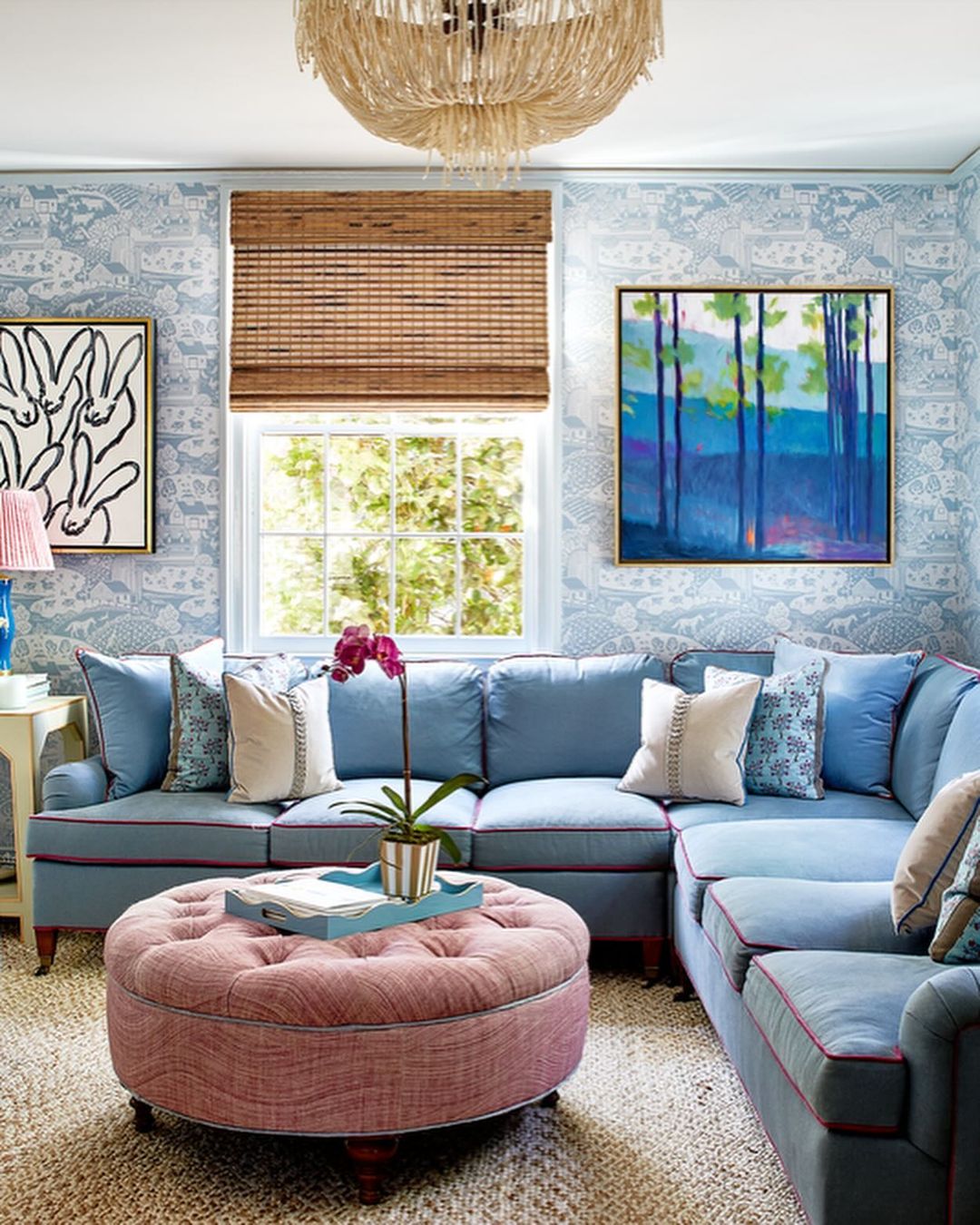 A cozy and vibrant living room featuring a plush blue sectional sofa and a contrasting pink tufted ottoman