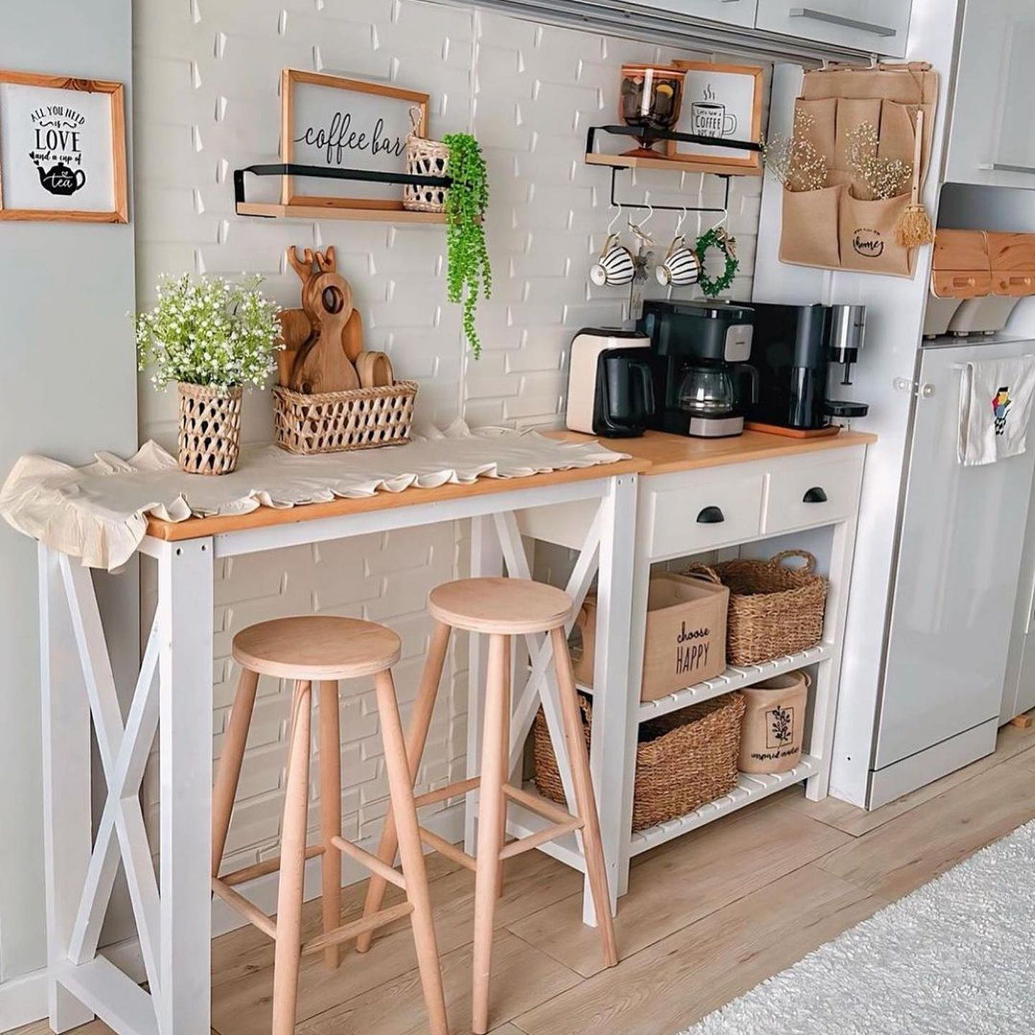 A neatly organized coffee corner featuring a white bar table, wooden stools, and decorative plants