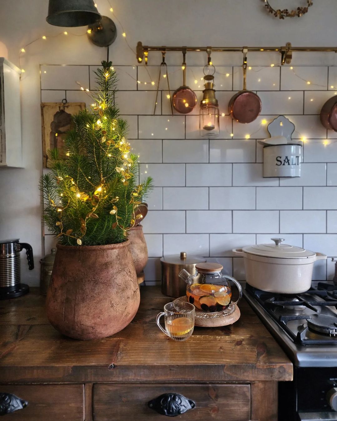 A cozy kitchen corner with a small pine tree adorned with sparkling lights, housed in a terracotta pot