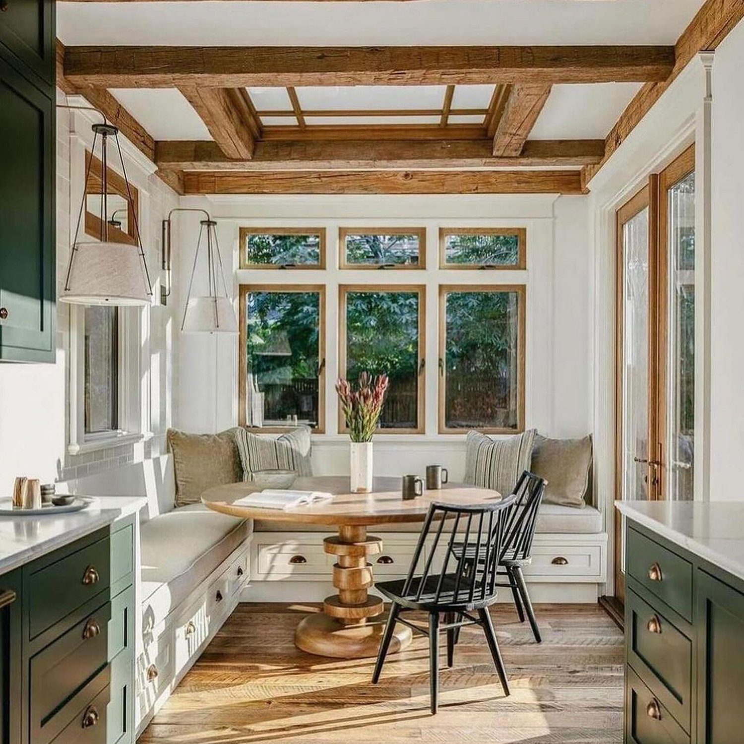 A cozy and inviting kitchen nook featuring exposed wooden beams, natural light, and subtle green cabinetry