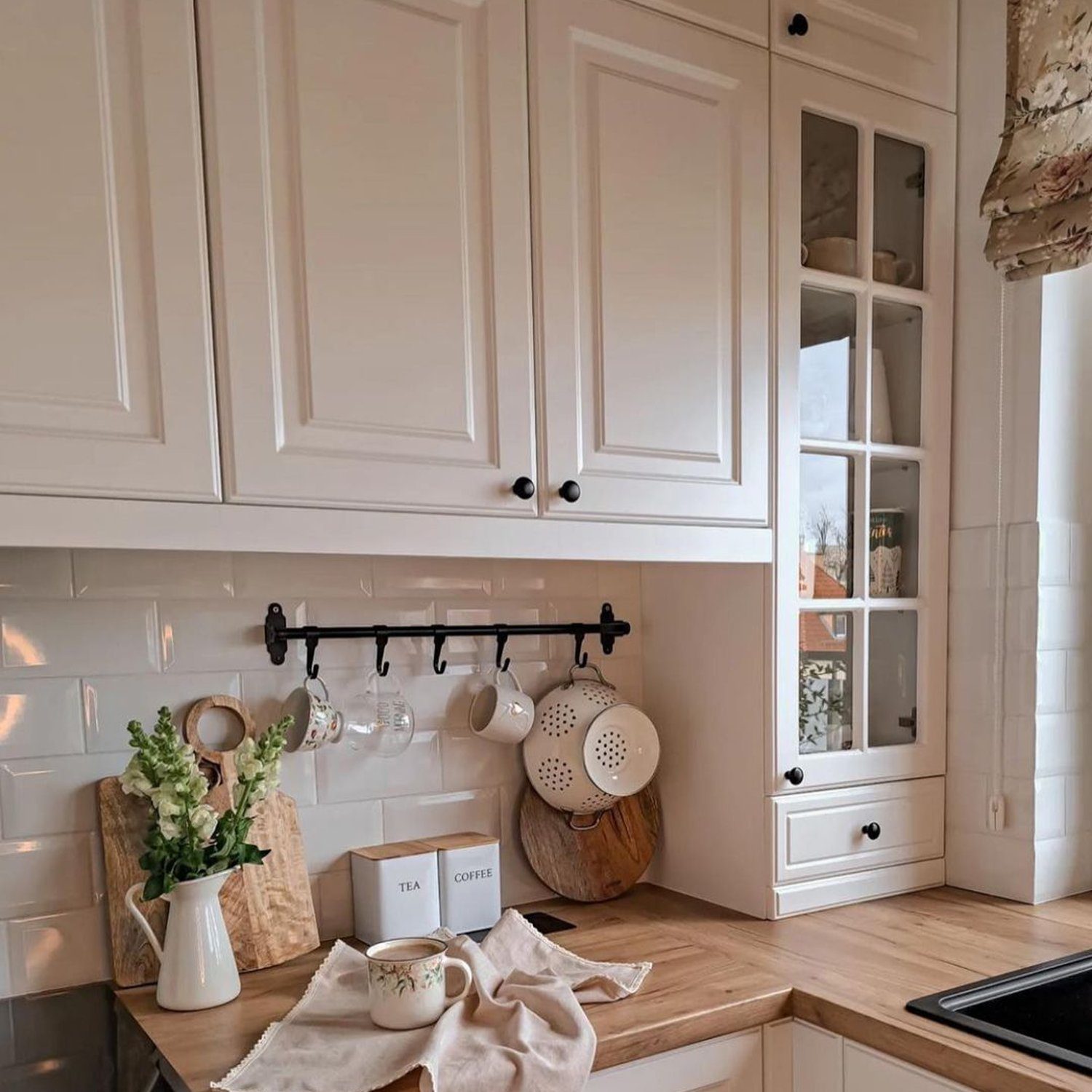 A neatly organized kitchen with white cabinetry, wooden countertops, and hanging utensils