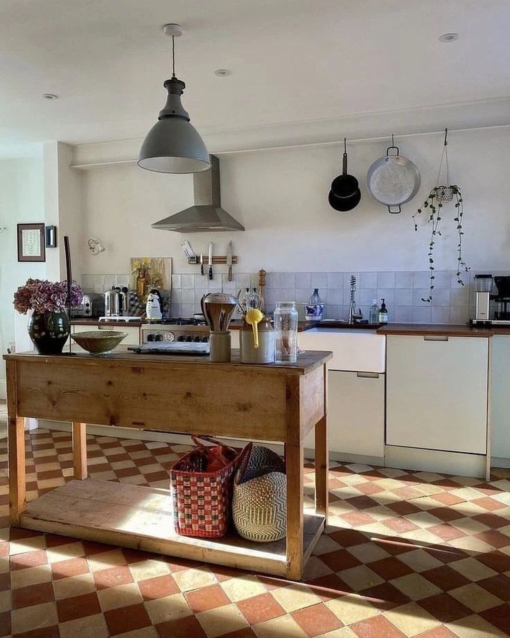 A warm and inviting kitchen featuring a rustic wooden table and terracotta-colored checkered floor.