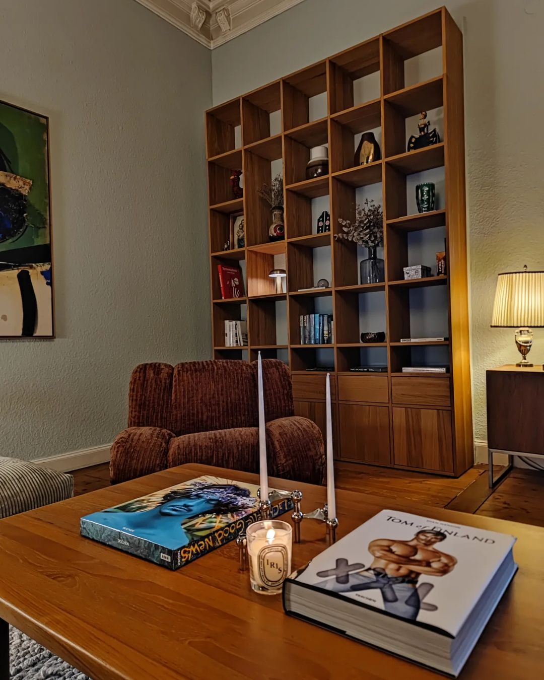 A cozy living room featuring a plush armchair and a wooden bookshelf brimming with various items