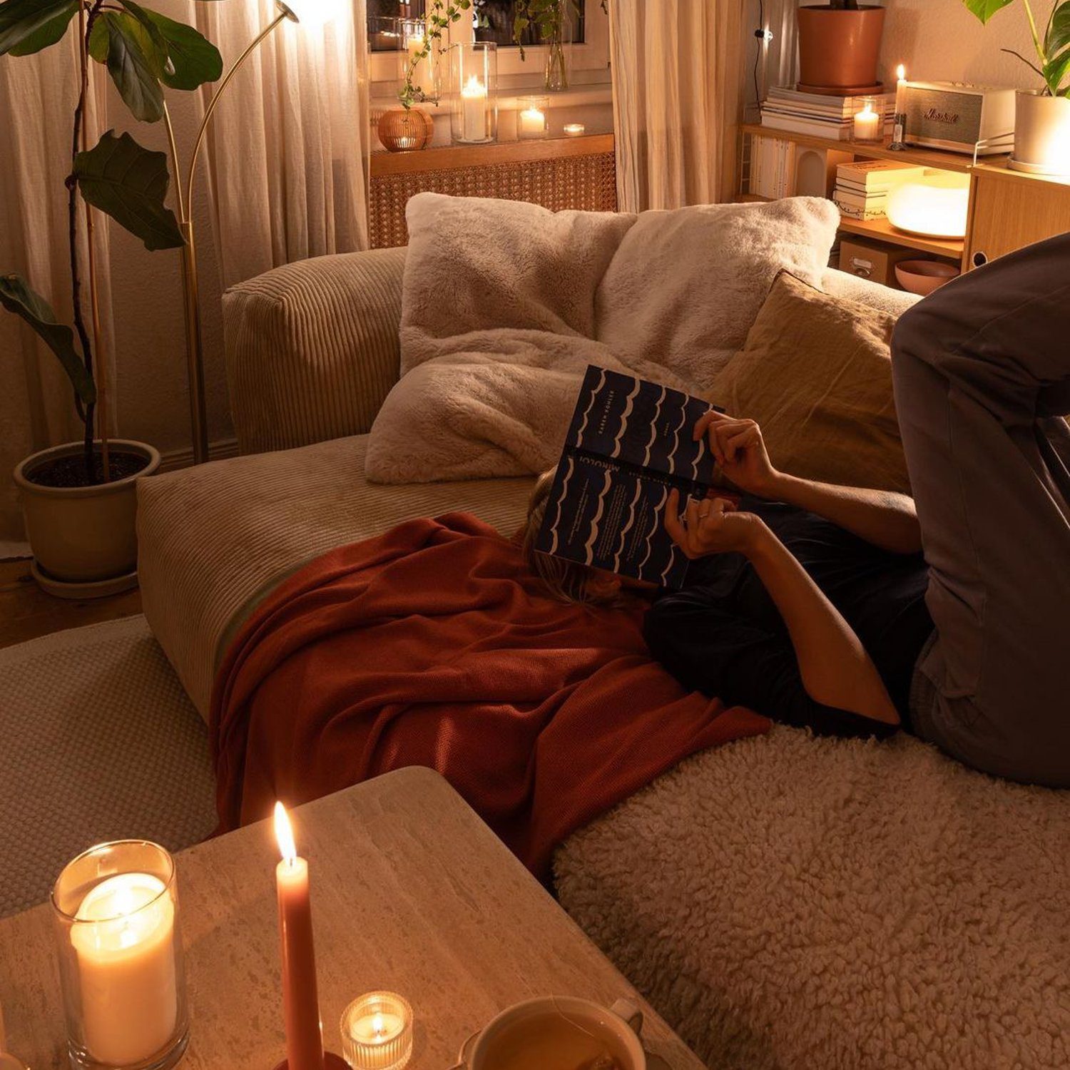 Cozy evening atmosphere with candles, a person reading on the couch, and warm lighting