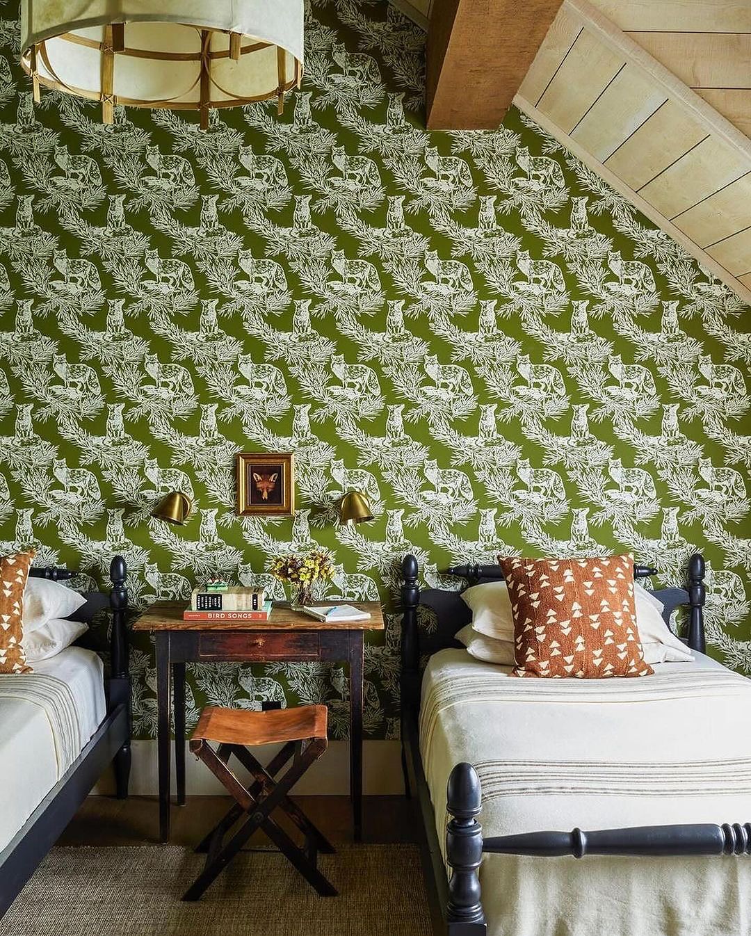 A cozy bedroom featuring twin beds with black posts contrasting against a vibrant green wallpaper decorated with white crane motifs