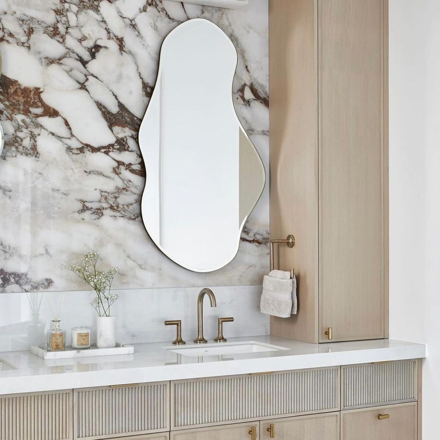 Elegant bathroom design featuring a unique shaped mirror and marble wall