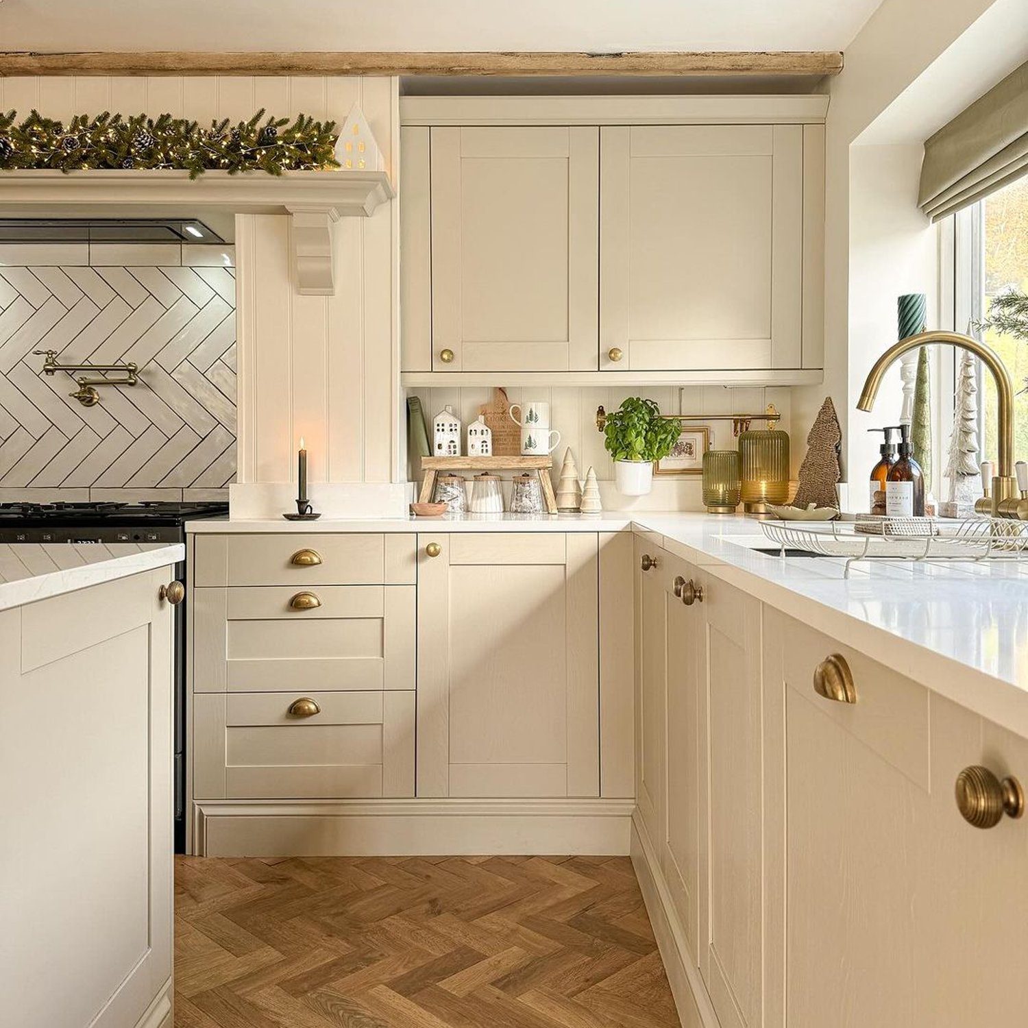 A warm and inviting kitchen featuring herringbone wood flooring, cream cabinetry, and brass hardware