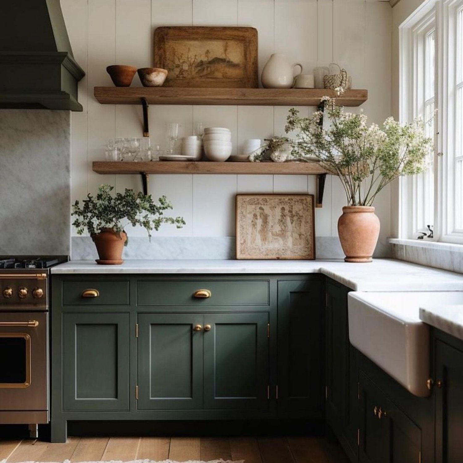 A classically styled kitchen featuring deep green cabinetry, brass hardware, and natural wood open shelving