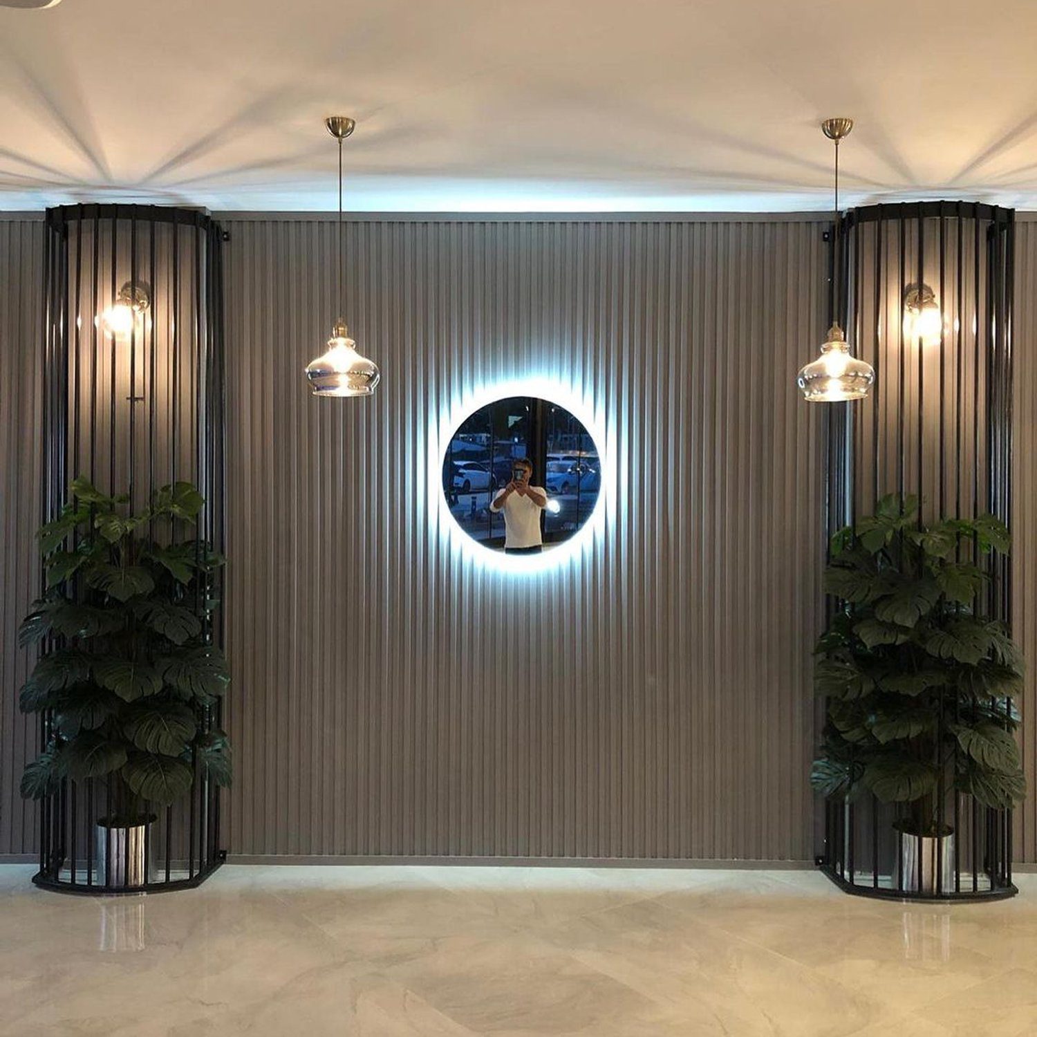 An elegantly designed interior space featuring a circular mirror with backlighting, flanked by vertical gardens and pendant lights.