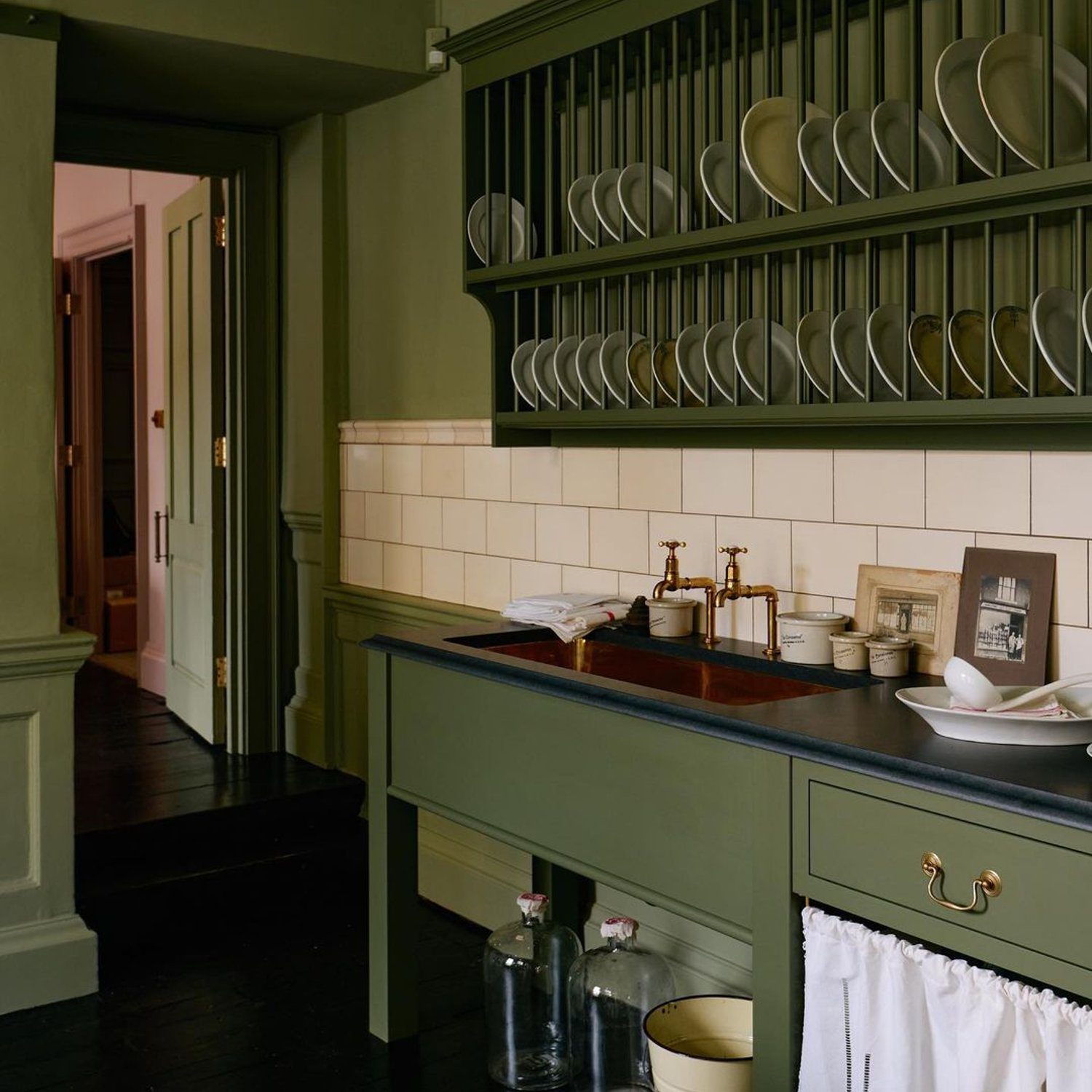 A meticulously organized kitchen with open shelving displaying a neat arrangement of plates and a deep green island counter