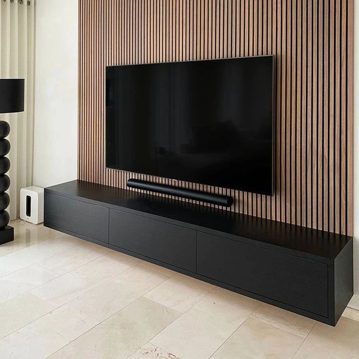 A sleek and modern living room featuring a wall-mounted TV against a wooden slatted backdrop and a minimalist black low-profile media console