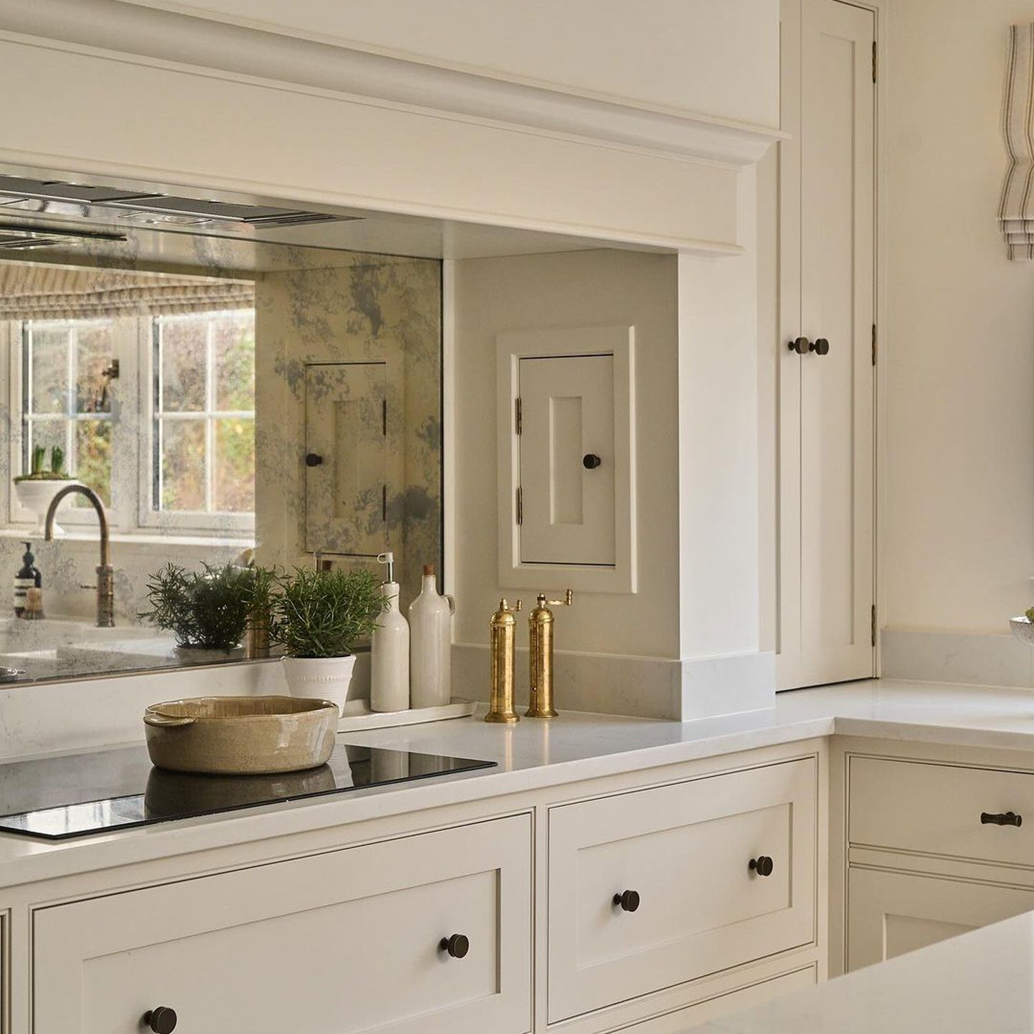 Elegant white kitchen design featuring a mirror backsplash and brass accents