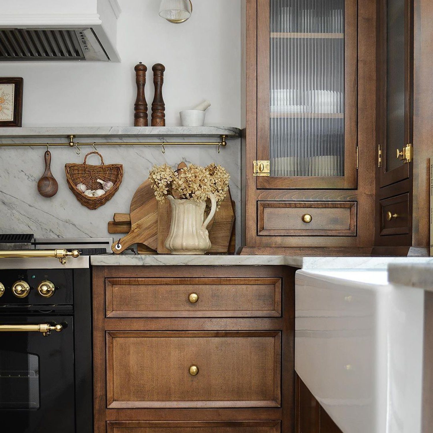 A sophisticated kitchen design showcasing warm wooden cabinets with brass hardware, complemented by marble countertops and backsplash, contrasted against a sleek black range with gold accents.