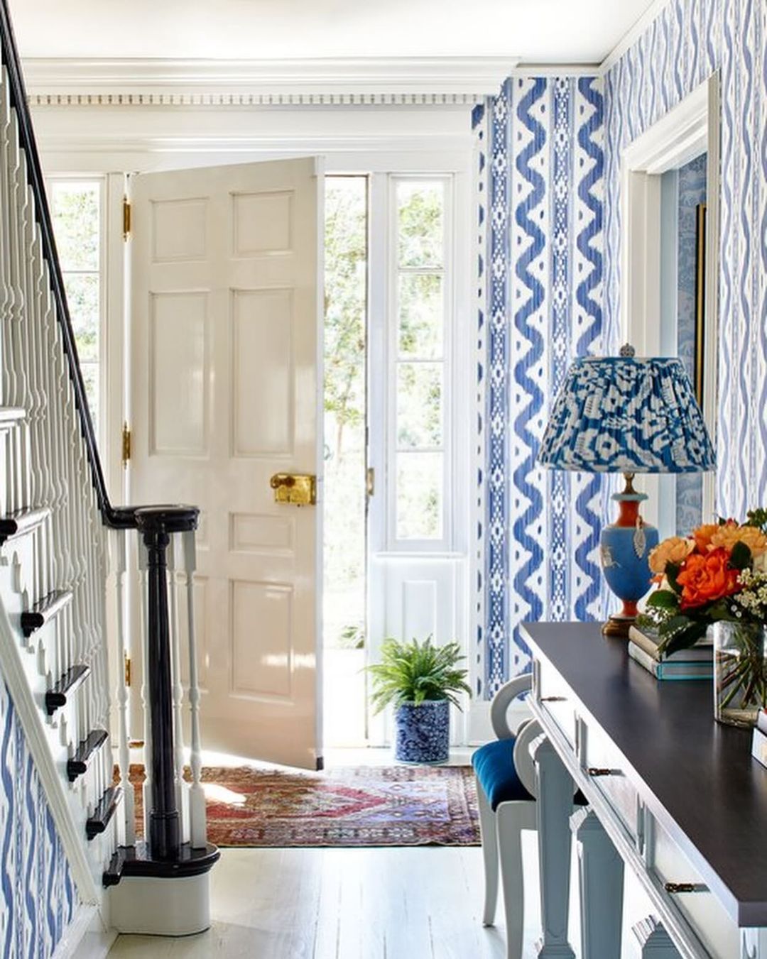 A welcoming entrance hall with striking blue geometric wallpaper and a classic black banister