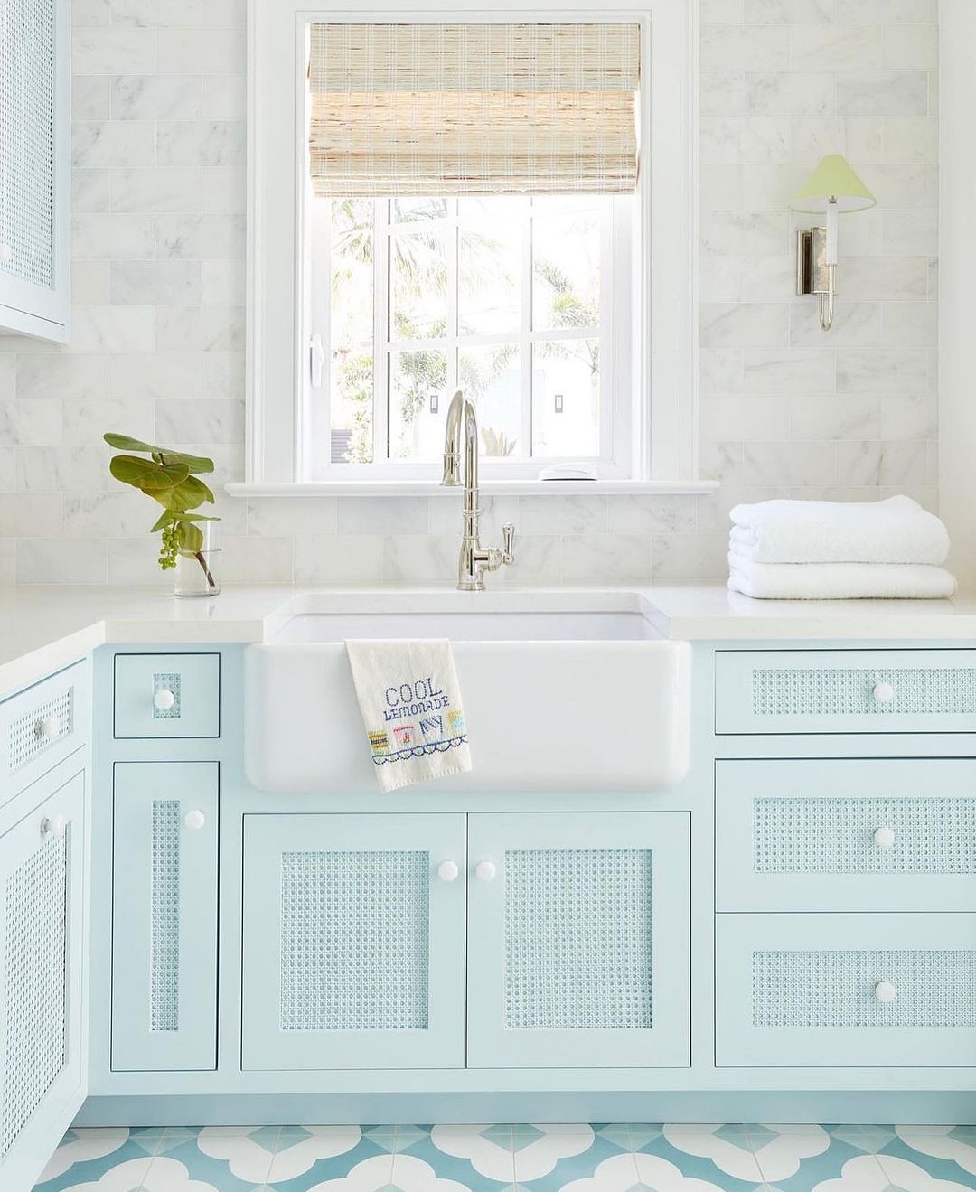 A fresh and inviting bathroom featuring a pastel blue vanity with lattice cabinet doors, paired with a crisp white farmhouse sink set against marble tiles.