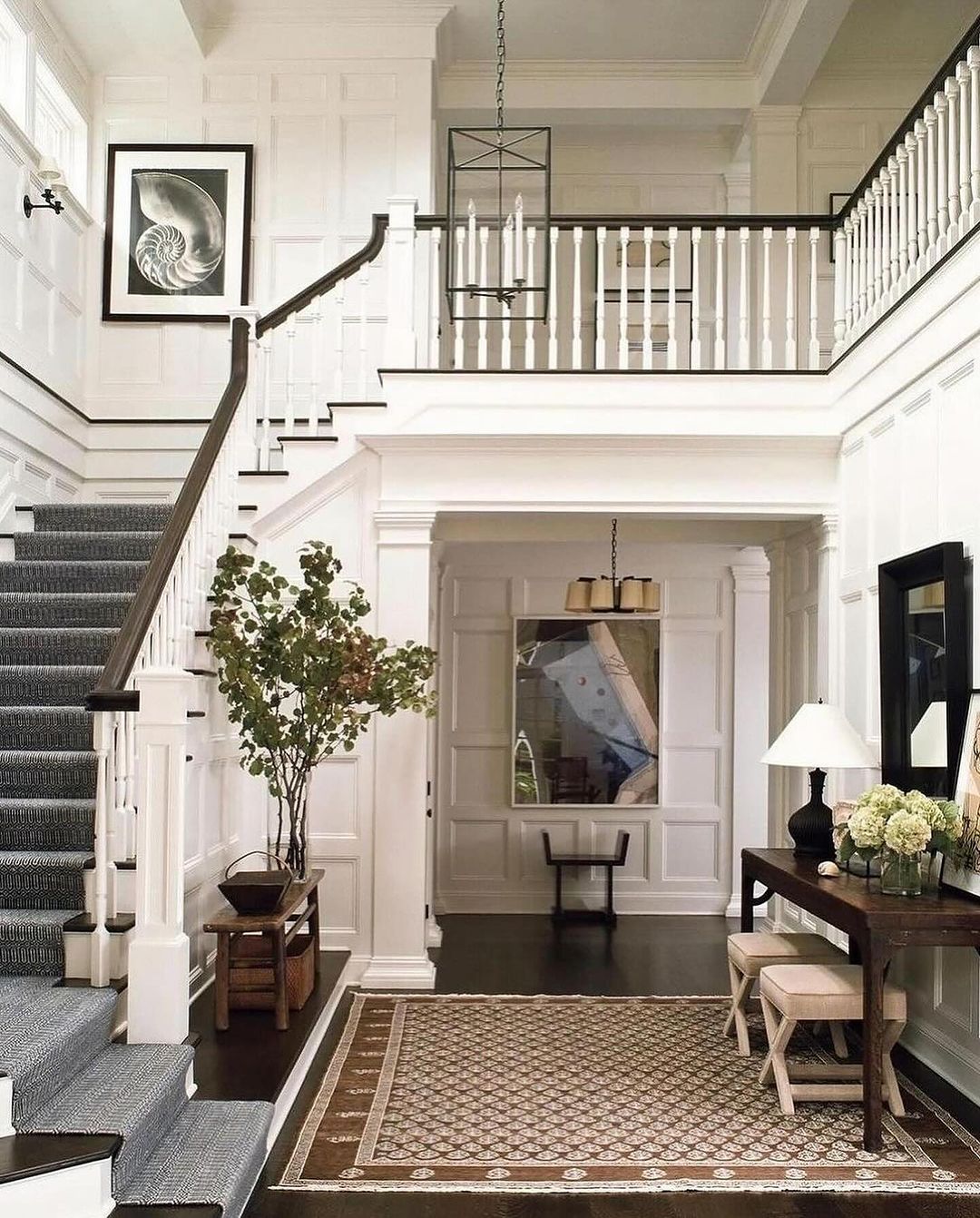 A classic grand entryway characterized by its high ceilings, white paneling, and dark hardwood floors