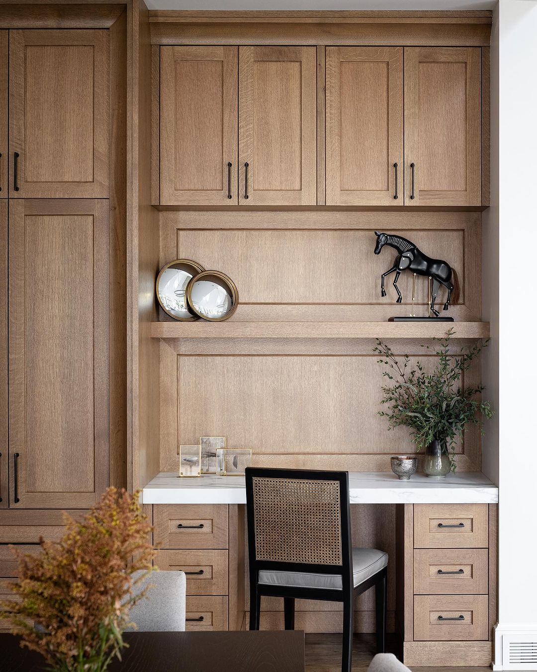 A tastefully designed home office nook featuring warm wood cabinetry and a woven black chair