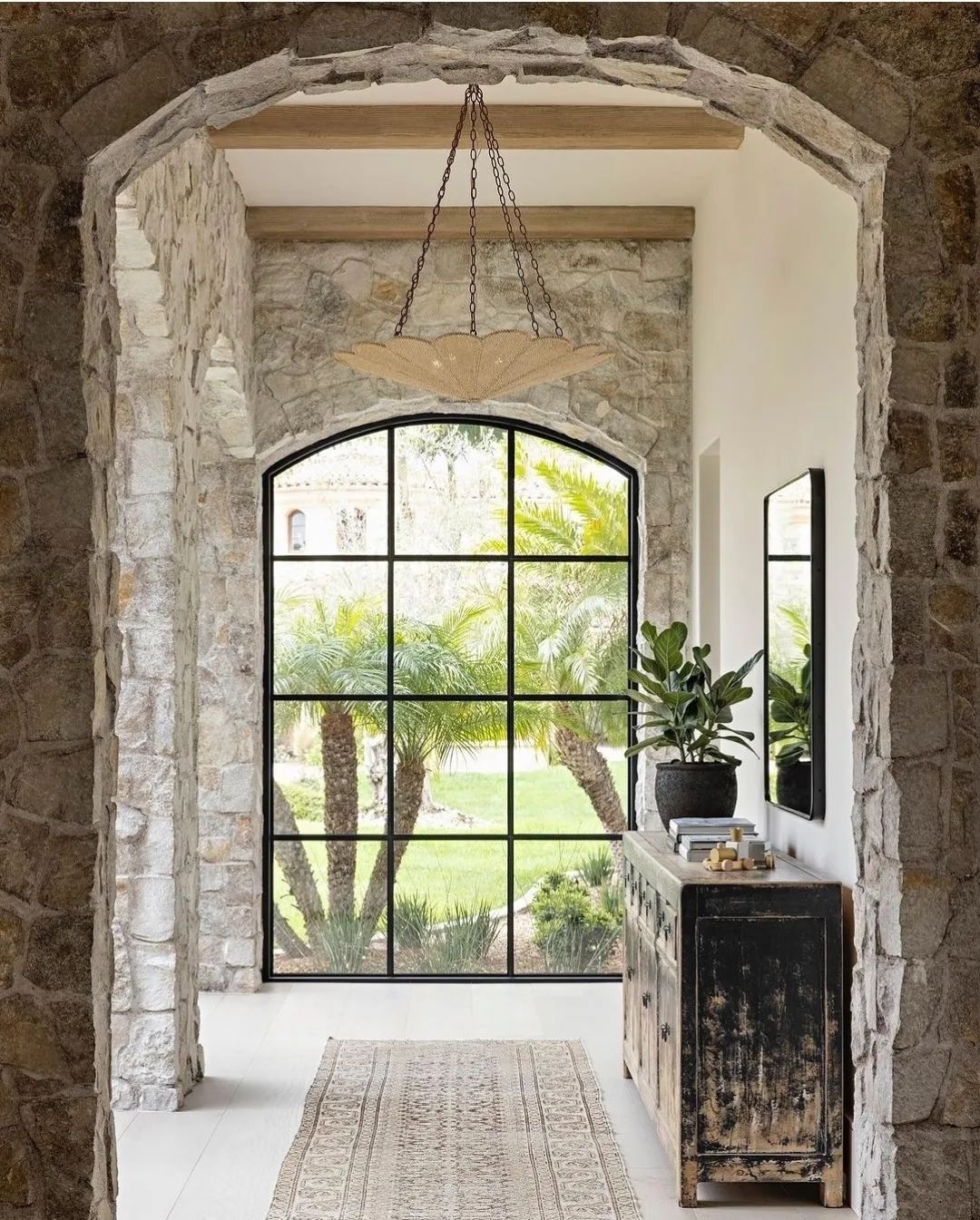 A harmonious blend of natural textures within an architectural space, featuring stone arches framing a panoramic window with a view of lush greenery.