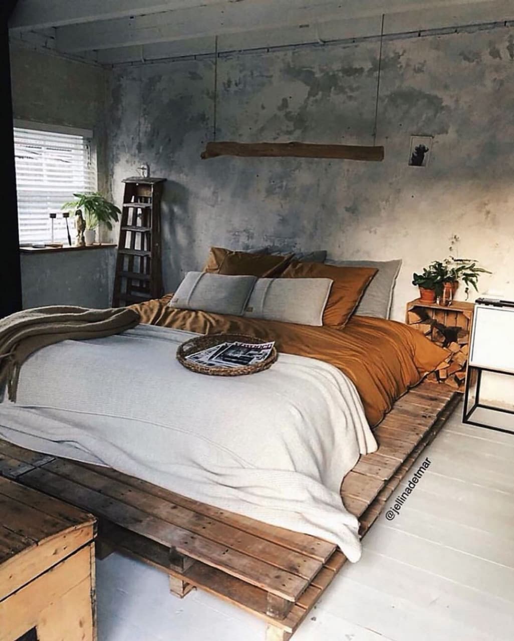 A ruggedly stylish bedroom embracing industrial chic with a bed mounted on pallet platforms and unfinished concrete walls.