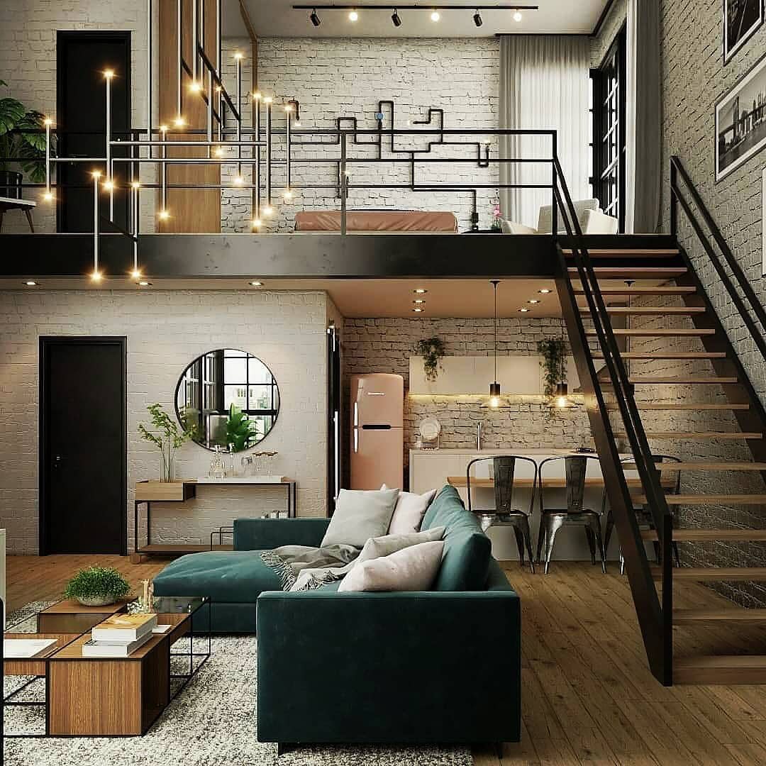 A chic and modern industrial loft featuring exposed brick walls, a bold green sofa, and a sleek black staircase leading to a cozy mezzanine bedroom.