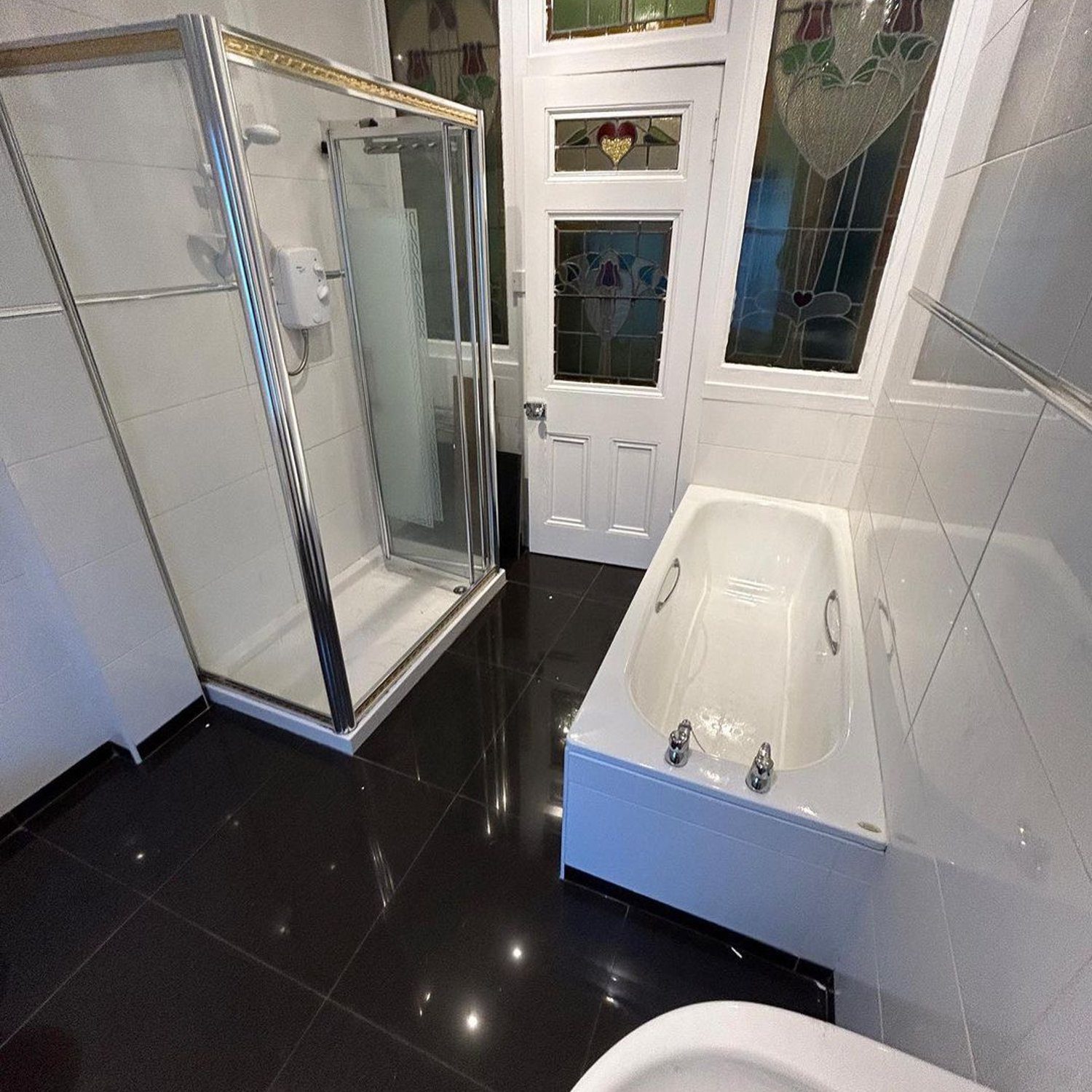 A modernly designed bathroom featuring sleek black floor tiles, pristine white wall tiles, and a combination of a glass-enclosed shower area alongside a compact bathtub.