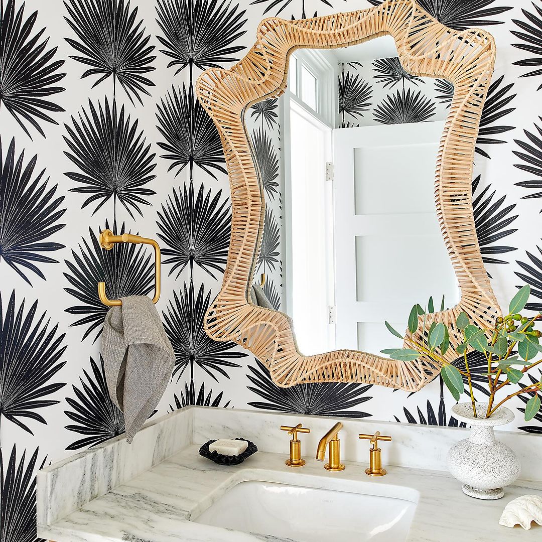 A strikingly bold bathroom featuring a wicker-framed mirror and tropical palm leaf wallpaper