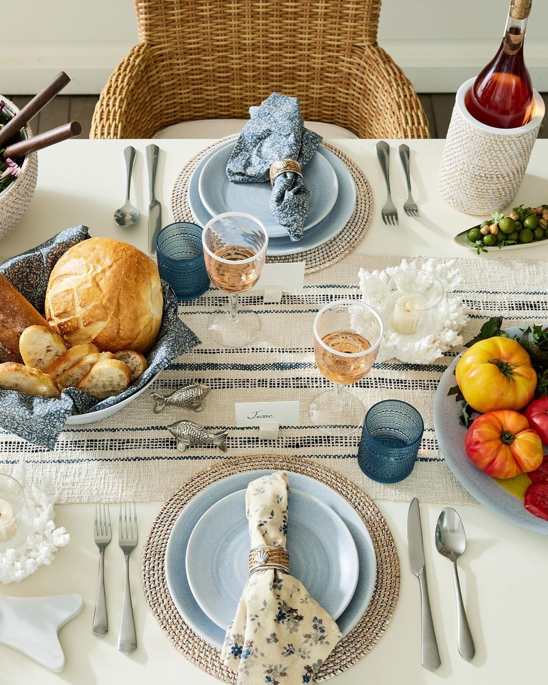 A beautifully set dining table with woven placemats, blue ceramic dishes, and a basket of fresh bread