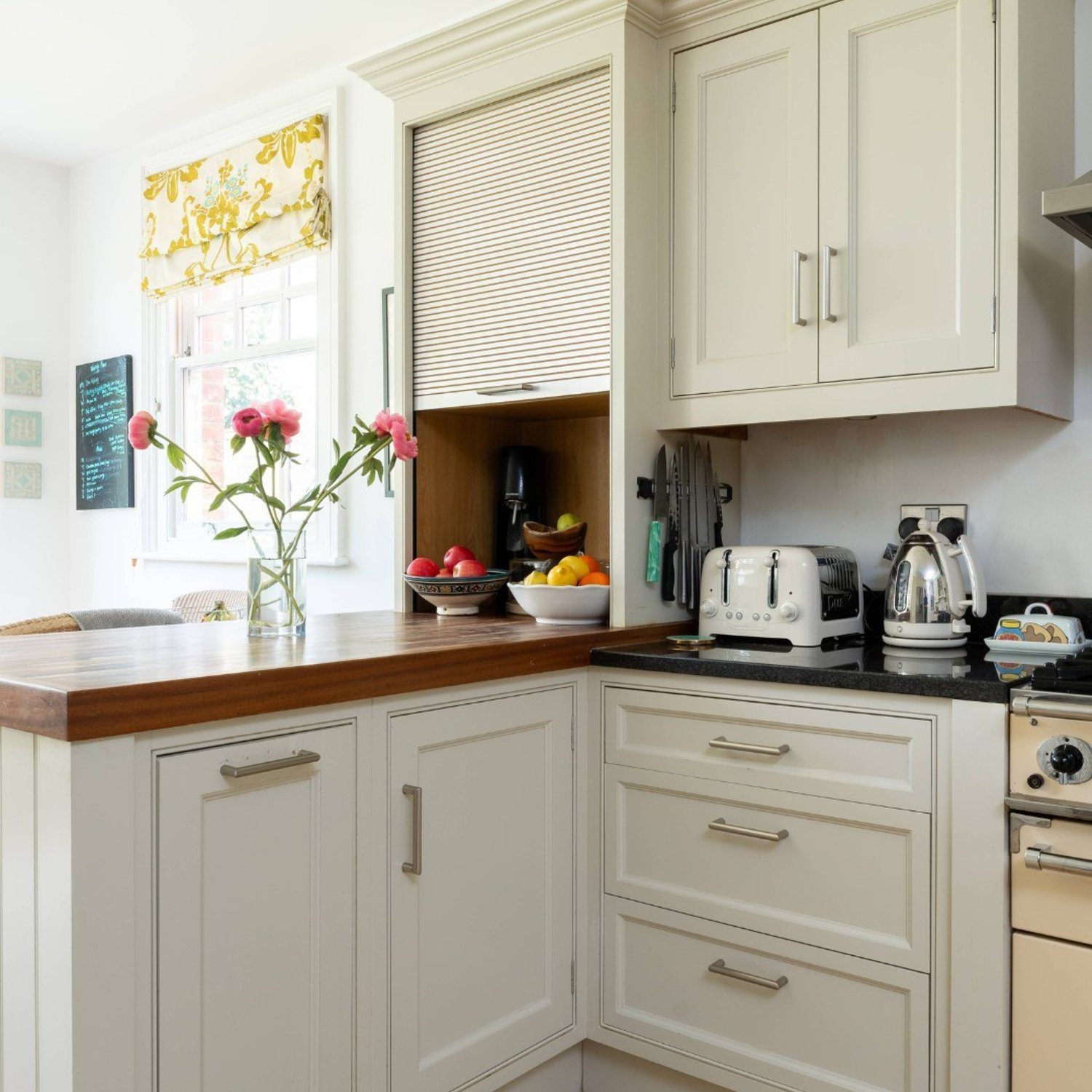 A cozy kitchen corner featuring classic cream cabinetry, a butcher block countertop, and pops of color from fresh flowers and fruits.