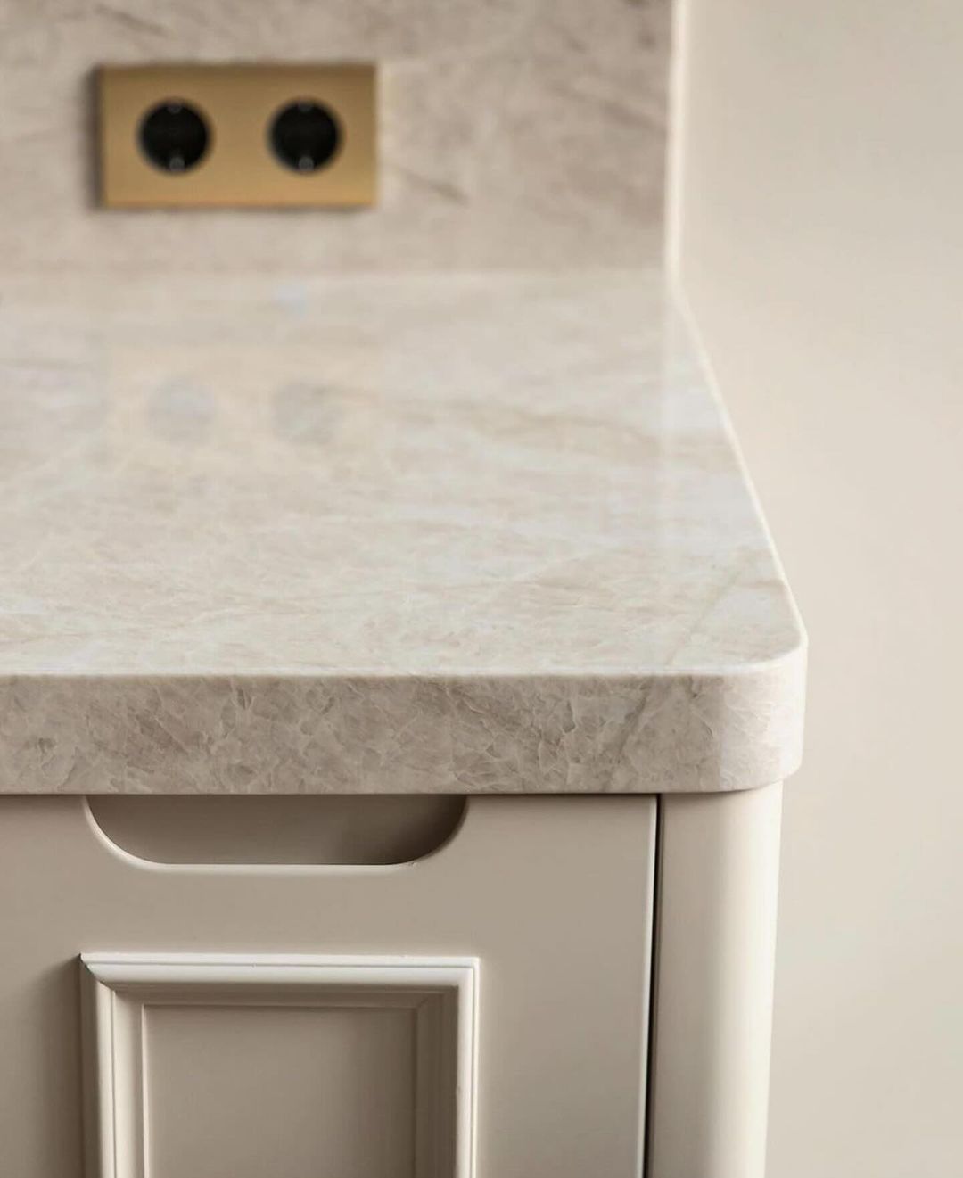 A minimalist kitchen corner featuring a marble countertop and chic white cabinetry with a stylish gold-finished power outlet