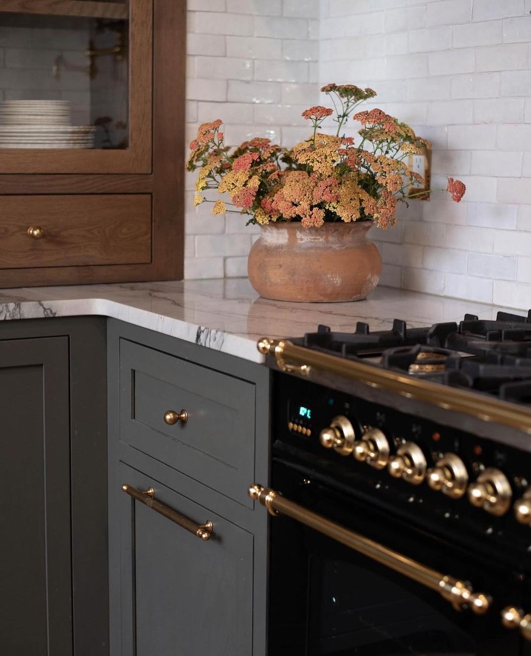 A tastefully arranged kitchen featuring a terracotta pot with vibrant flowers, against a white tiled backsplash