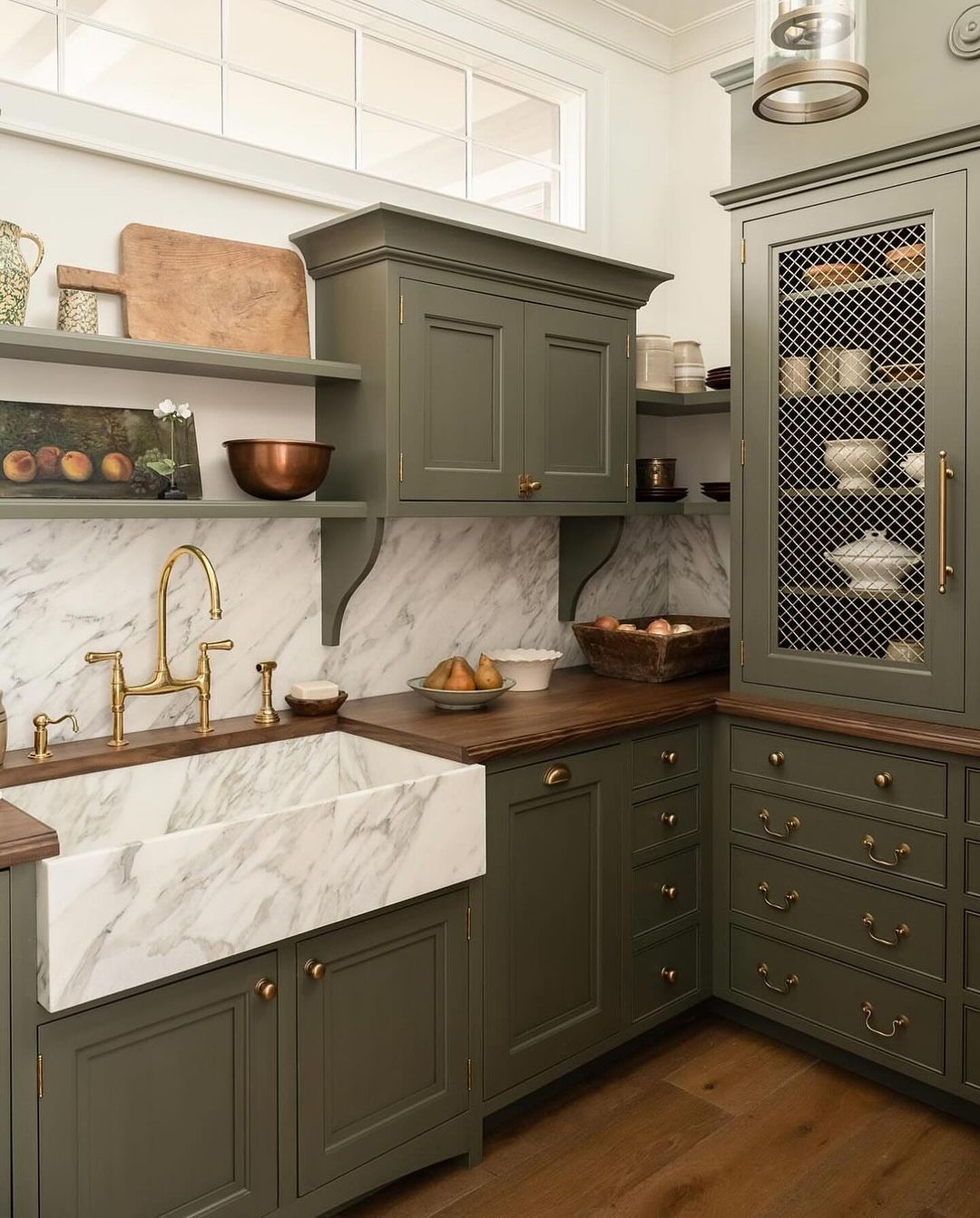 A modern kitchen with dark green cabinetry, brass hardware, and marble countertops