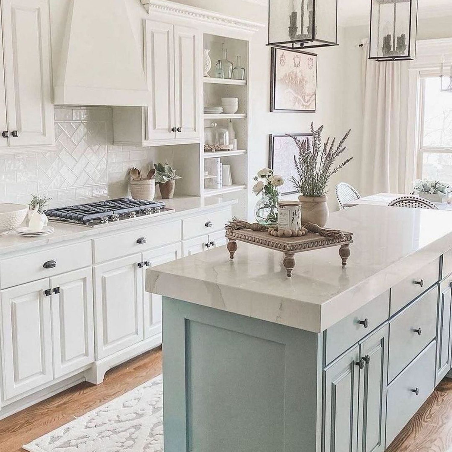 Elegant white and hints of pale blue kitchen featuring a large central island, open shelving, and lantern style pendant lights