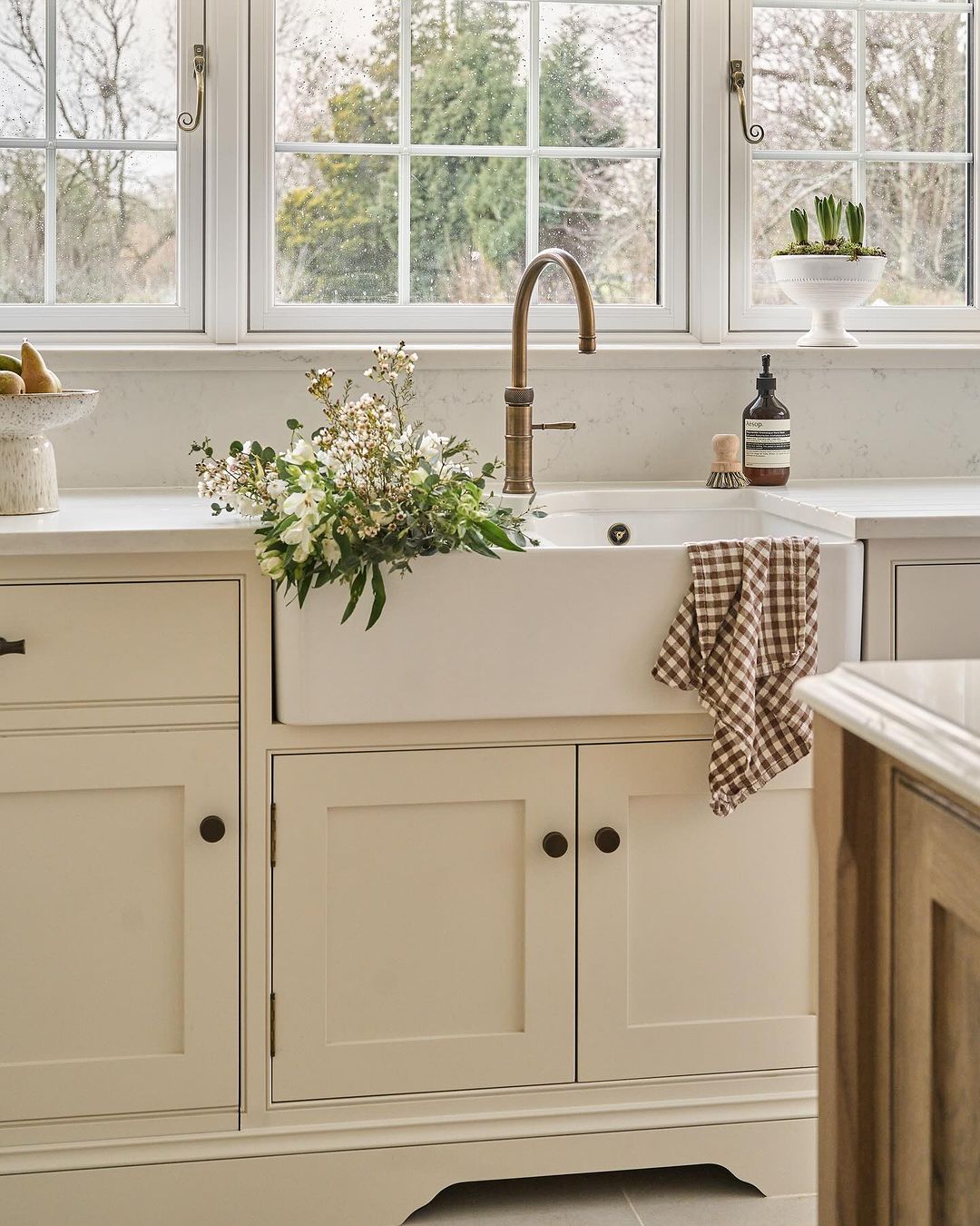 A warm and inviting kitchen setting featuring a farmhouse sink with a bronze faucet, set against white cabinetry and marble countertops