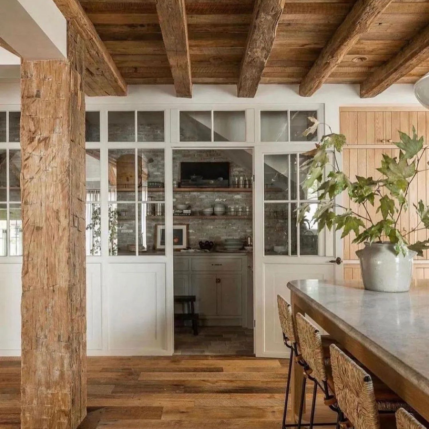 A rustic-modern kitchen space featuring exposed wooden beams and a French glass door partition