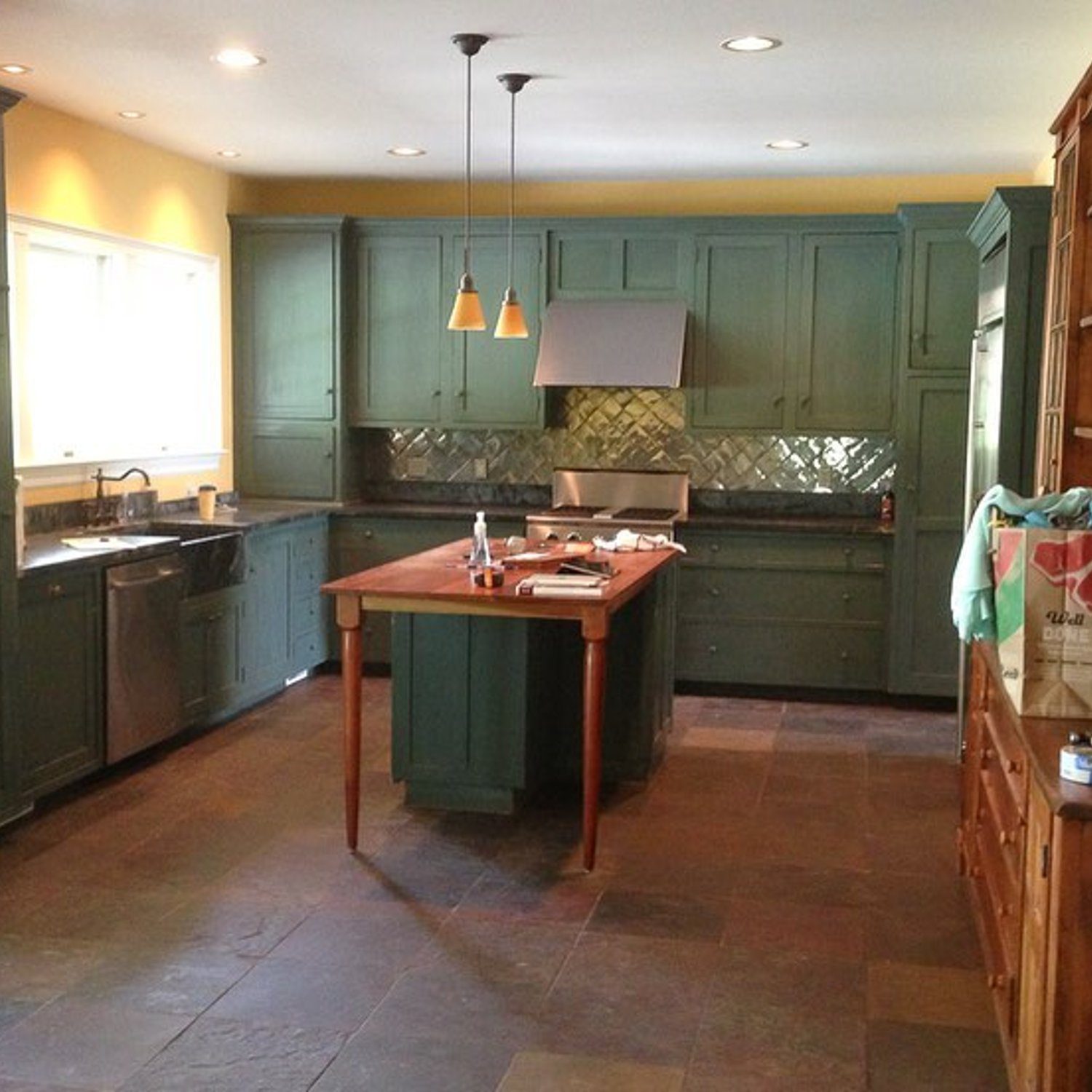 A rustic kitchen with slate floor tiles and olive green cabinetry