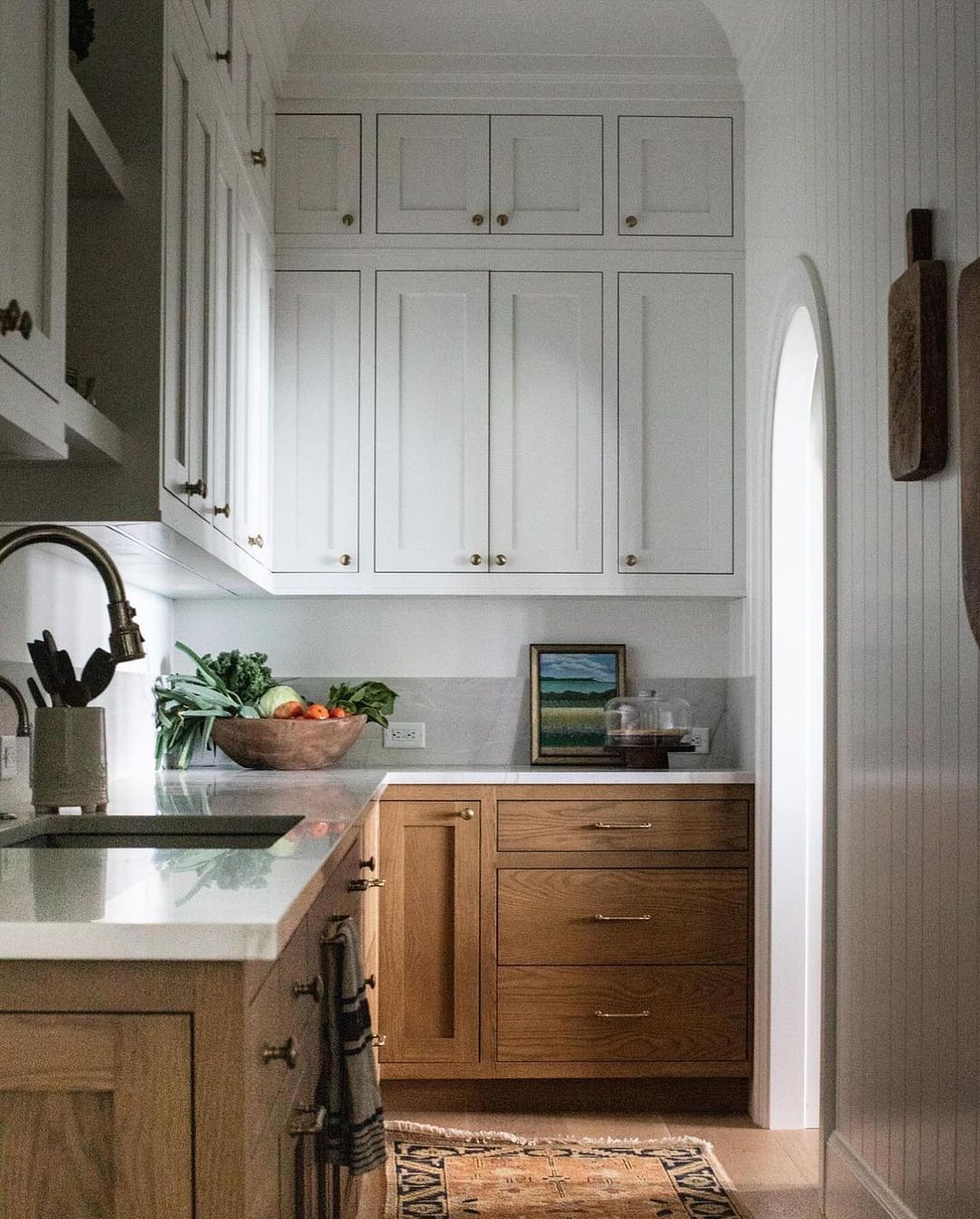 A harmonious blend of traditional and modern elements defines this kitchen space featuring white cabinetry with brass hardware, wood base cabinets, and a classic subway tile backsplash.