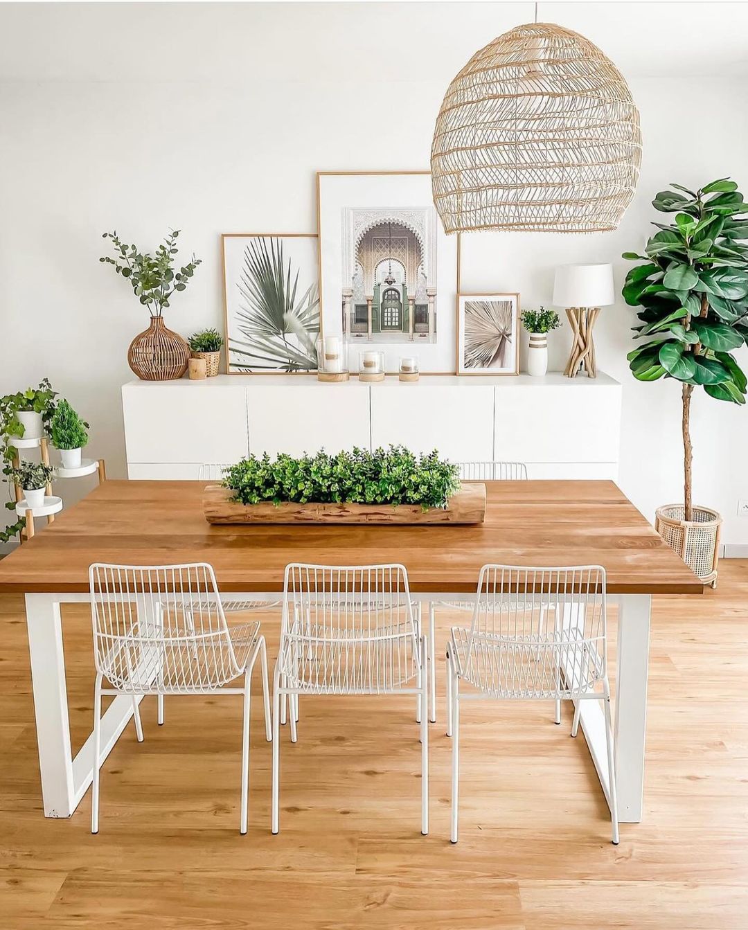 A minimalist dining room with white walls, light wooden flooring, and abundant greenery