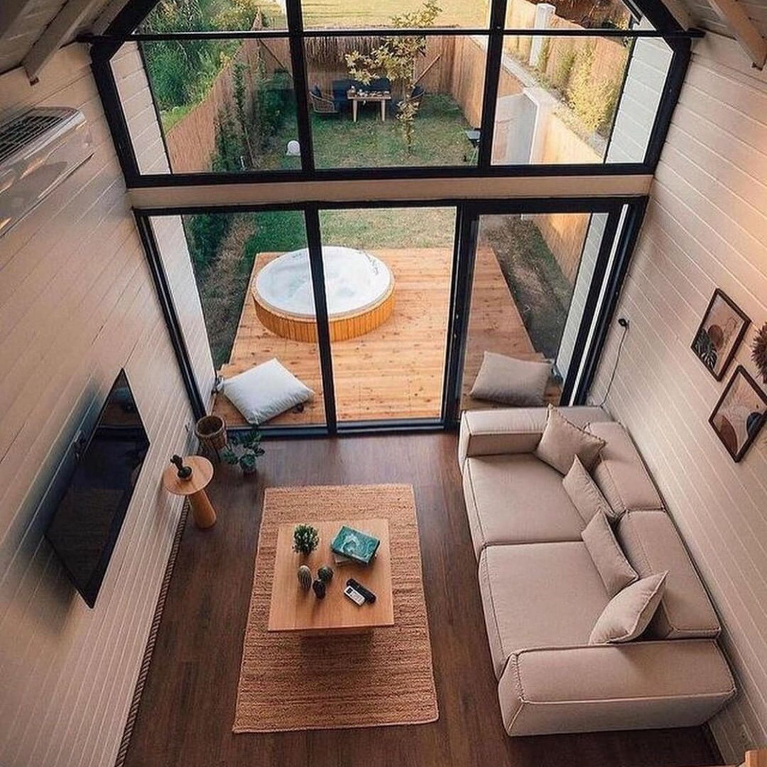 A modern A-frame cabin interior with a cozy living area and large windows overlooking a hot tub and scenic outdoor view.