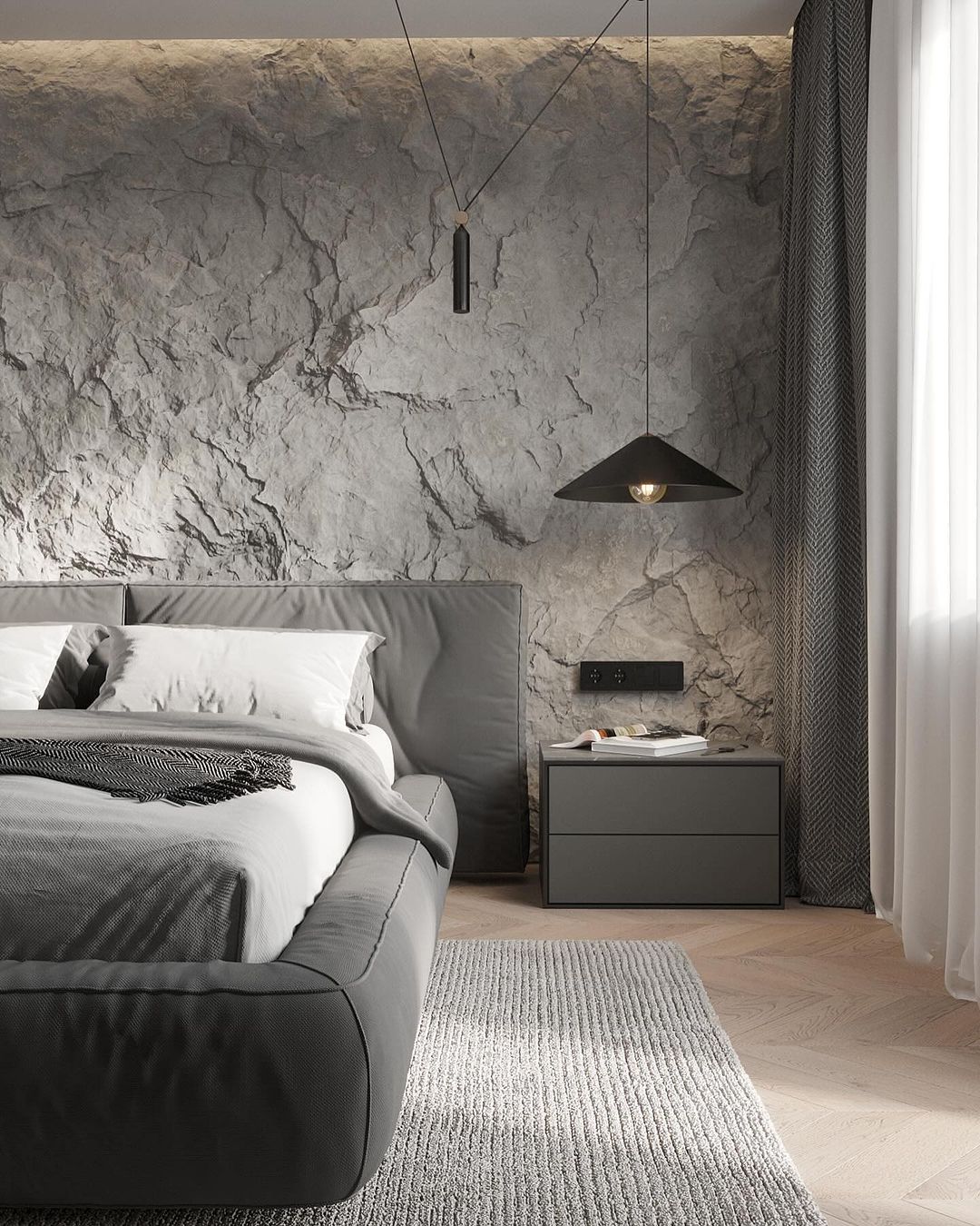 A modern bedroom featuring a plush gray bed against a textured gray stone wall, with chic pendant lighting providing a warm ambiance.