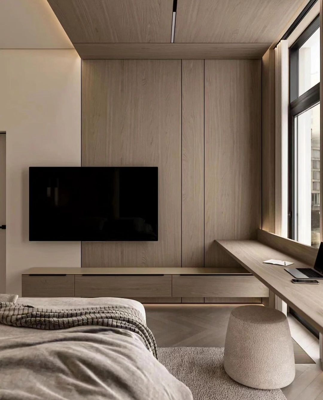 A contemporary minimalist bedroom featuring integrated wooden cabinetry with a flush-mounted TV, a streamlined desk and stool, complemented by understated bedding textures.