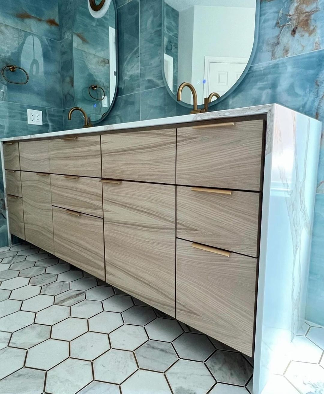 A modern bathroom sporting hexagonal white tiles with gray grouting, complementing a sleek wooden vanity and chic blue marbled walls.