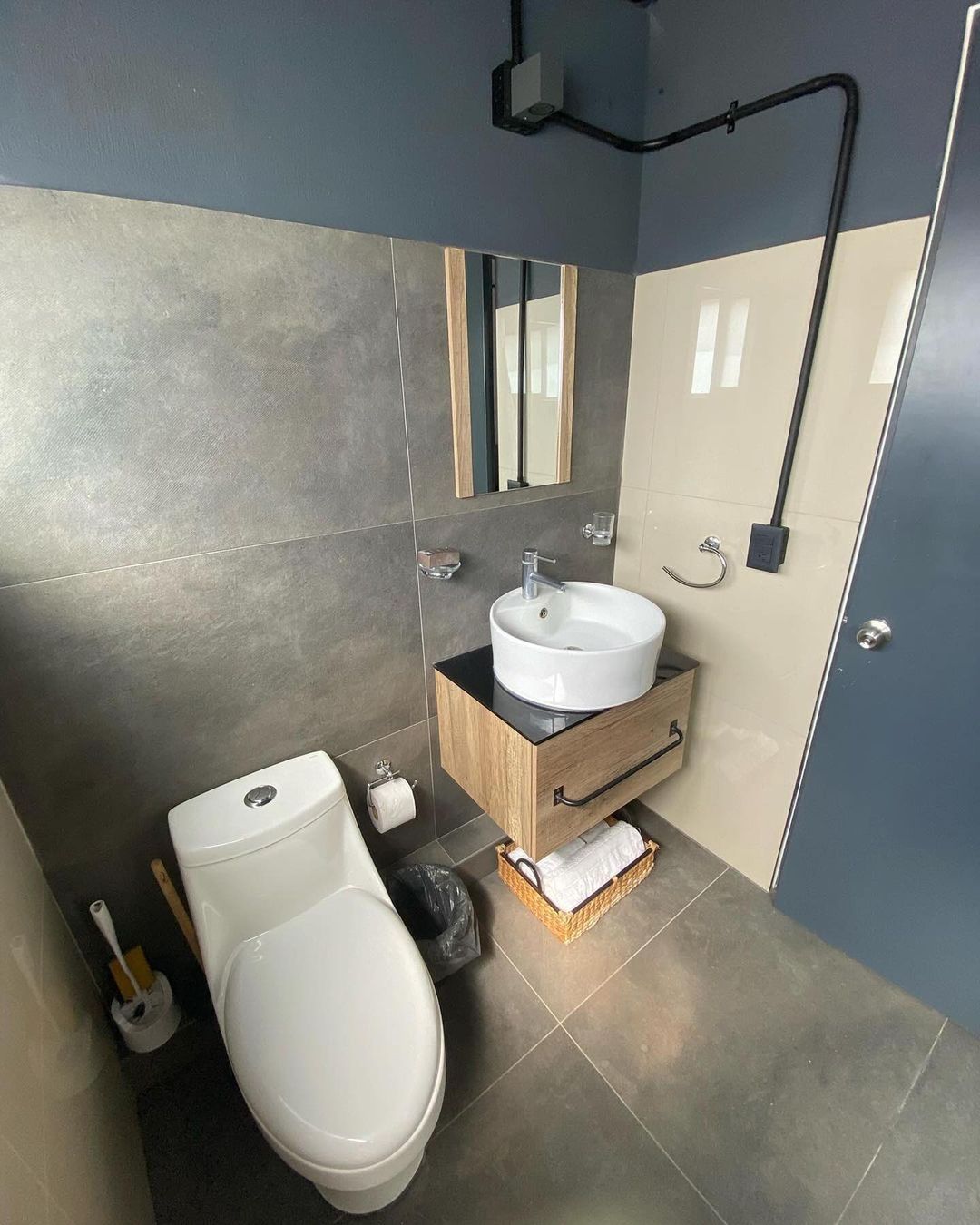 A chic modern bathroom showcasing dark grey tiles, a wooden vanity with a vessel sink, and a minimalist mirror