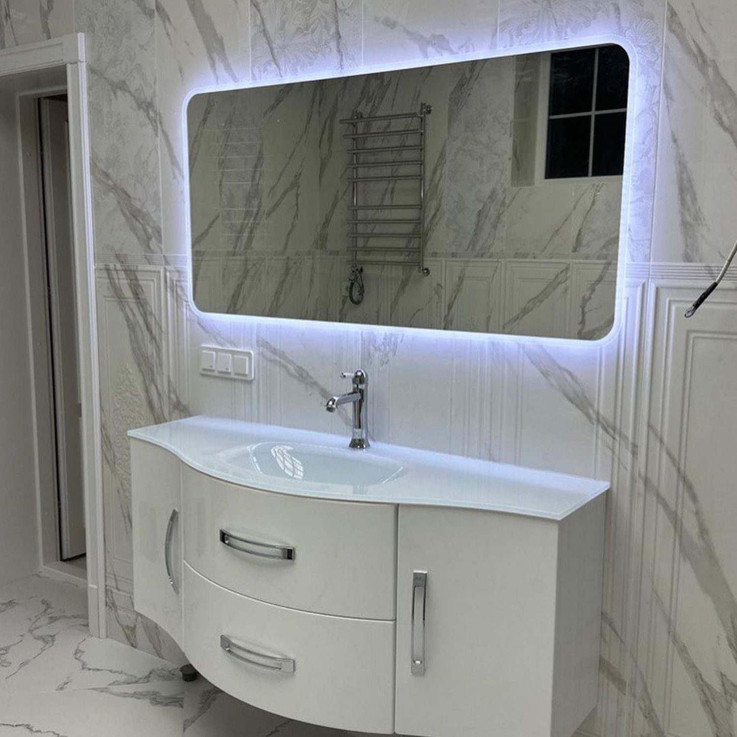 Elegant and modern bathroom design featuring marble-patterned walls, a curved floating vanity, and an illuminated mirror